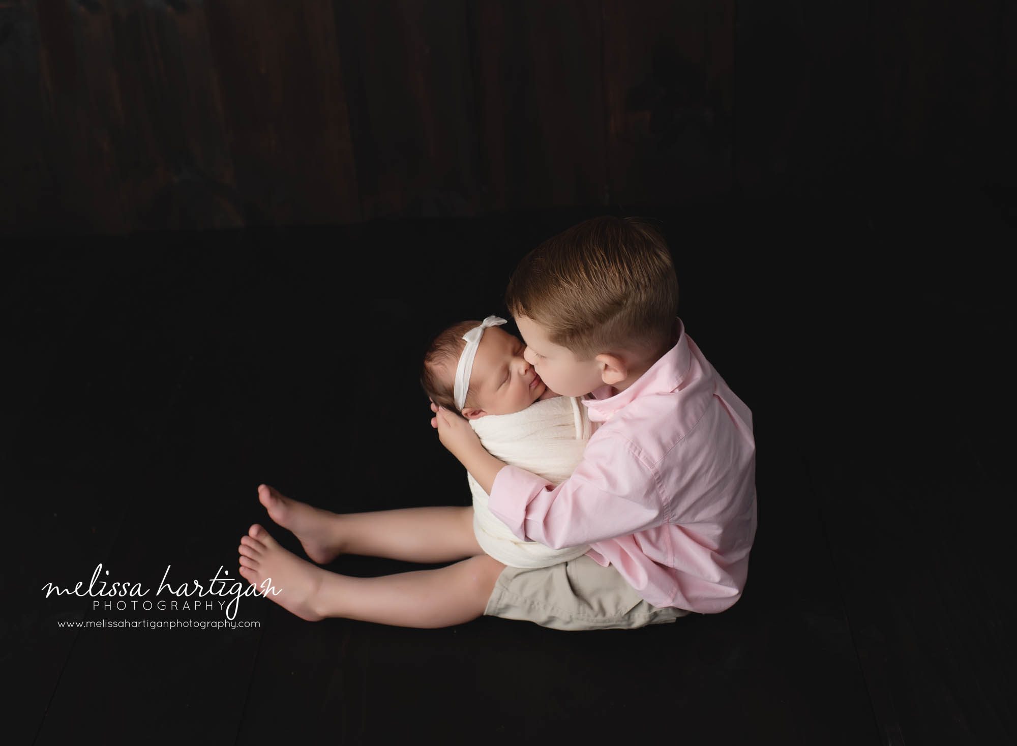 toddler boy giving newborn baby sister a kiss studio newborn photography