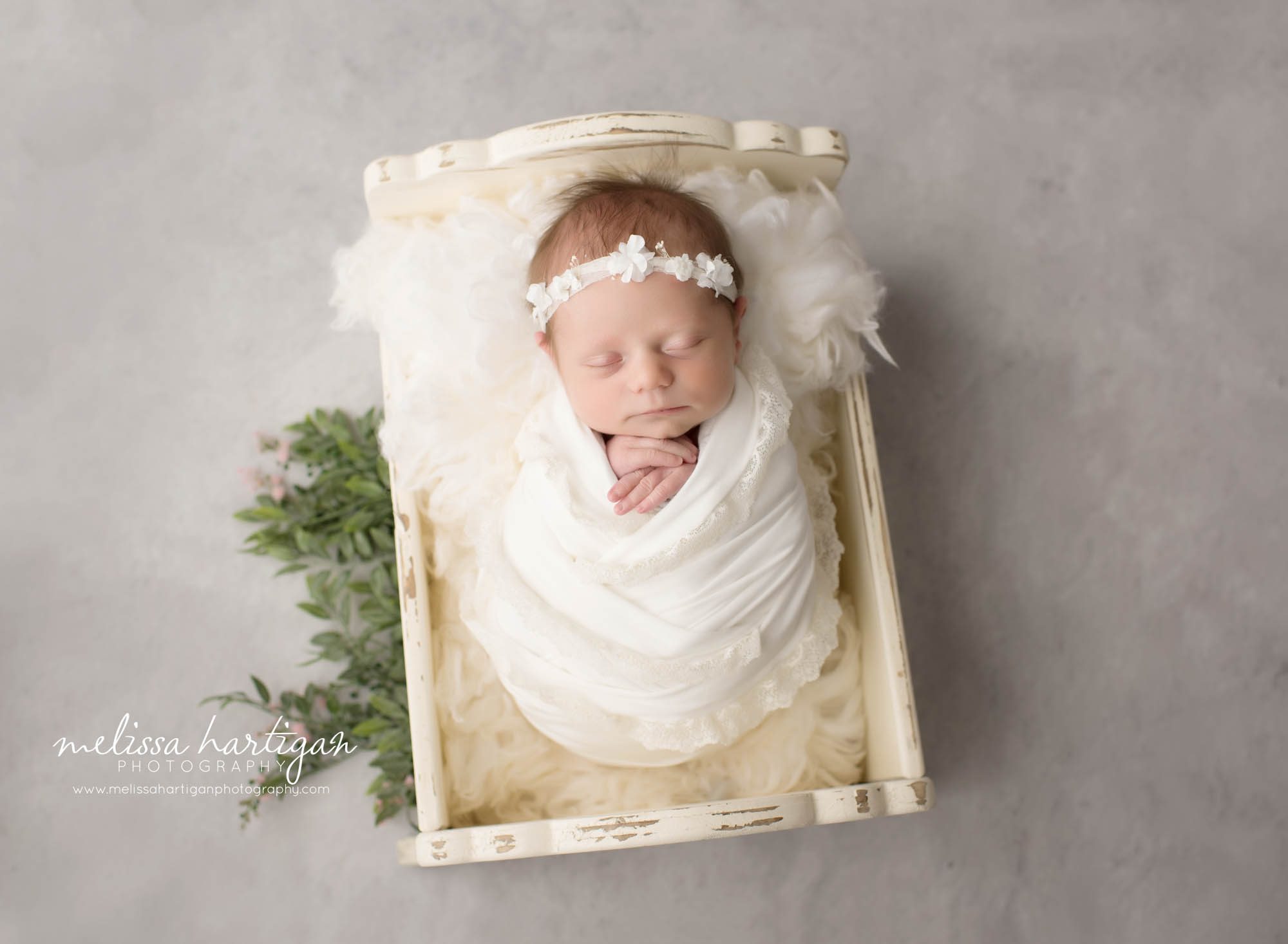 newborn baby girl wrapped in cream wrap posed in wooden cradle