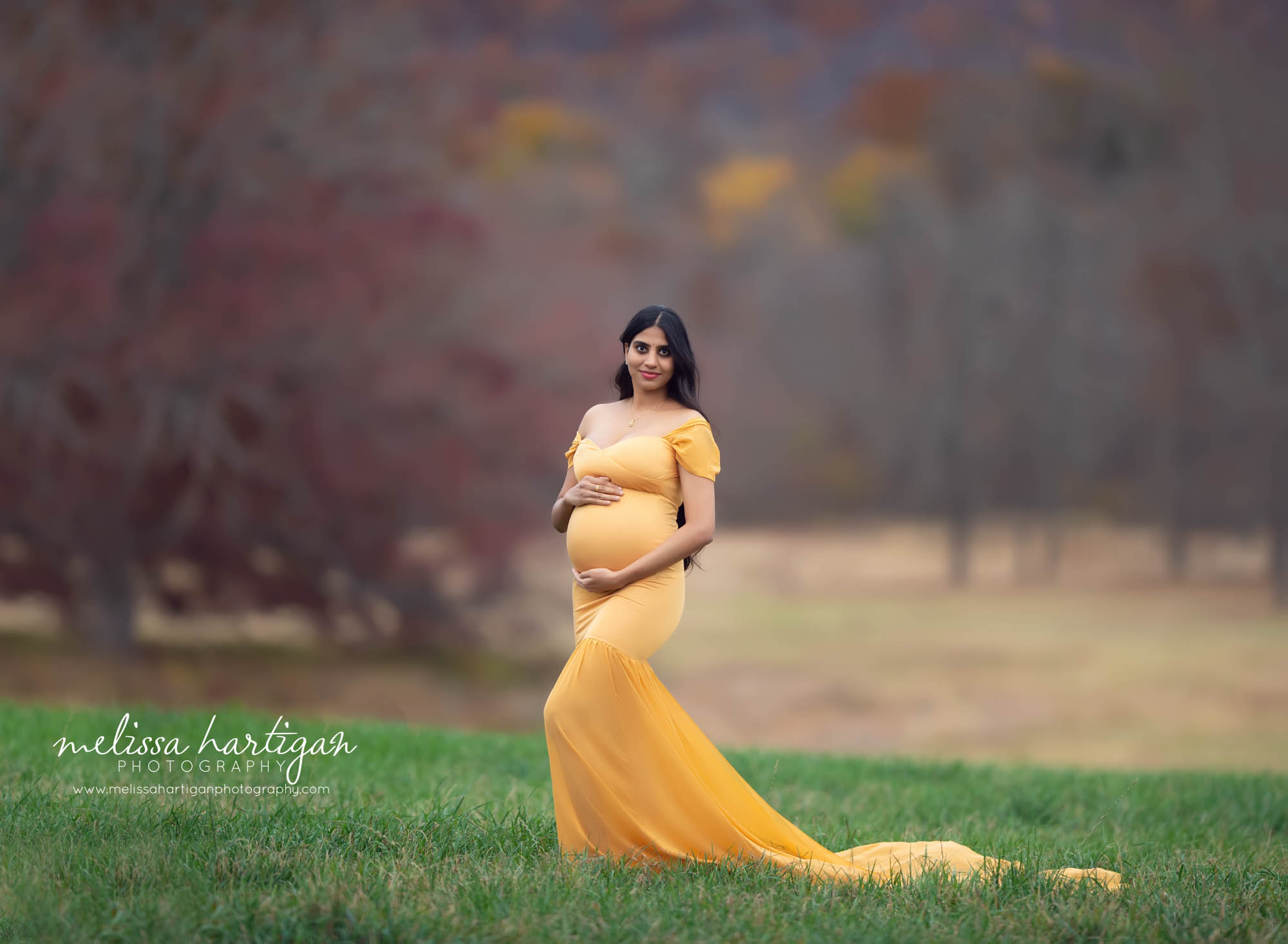 Mom to be standing outside fall maternity picture wearing orange colored long form fitting maternity gown maternity photography ct
