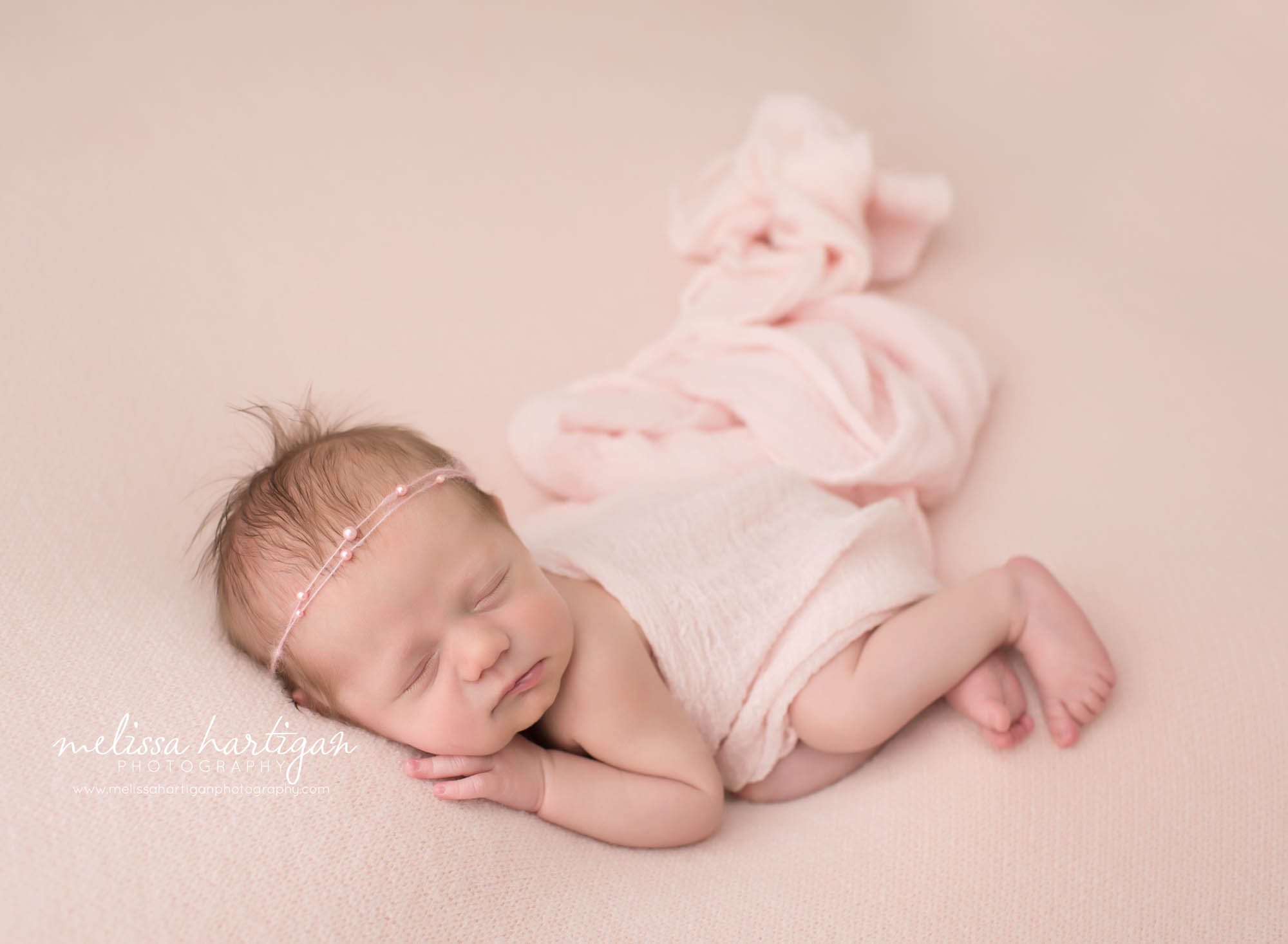 newborn baby girl posed on side with pink wrap draped over baby Newborn Photographer Massachusetts