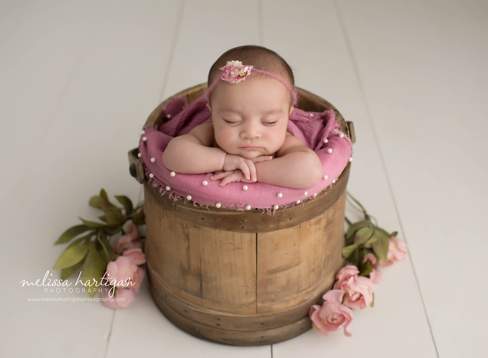 Newborn baby girl posed in wooden bucket prop with pink layer and pink flowerstieback headband