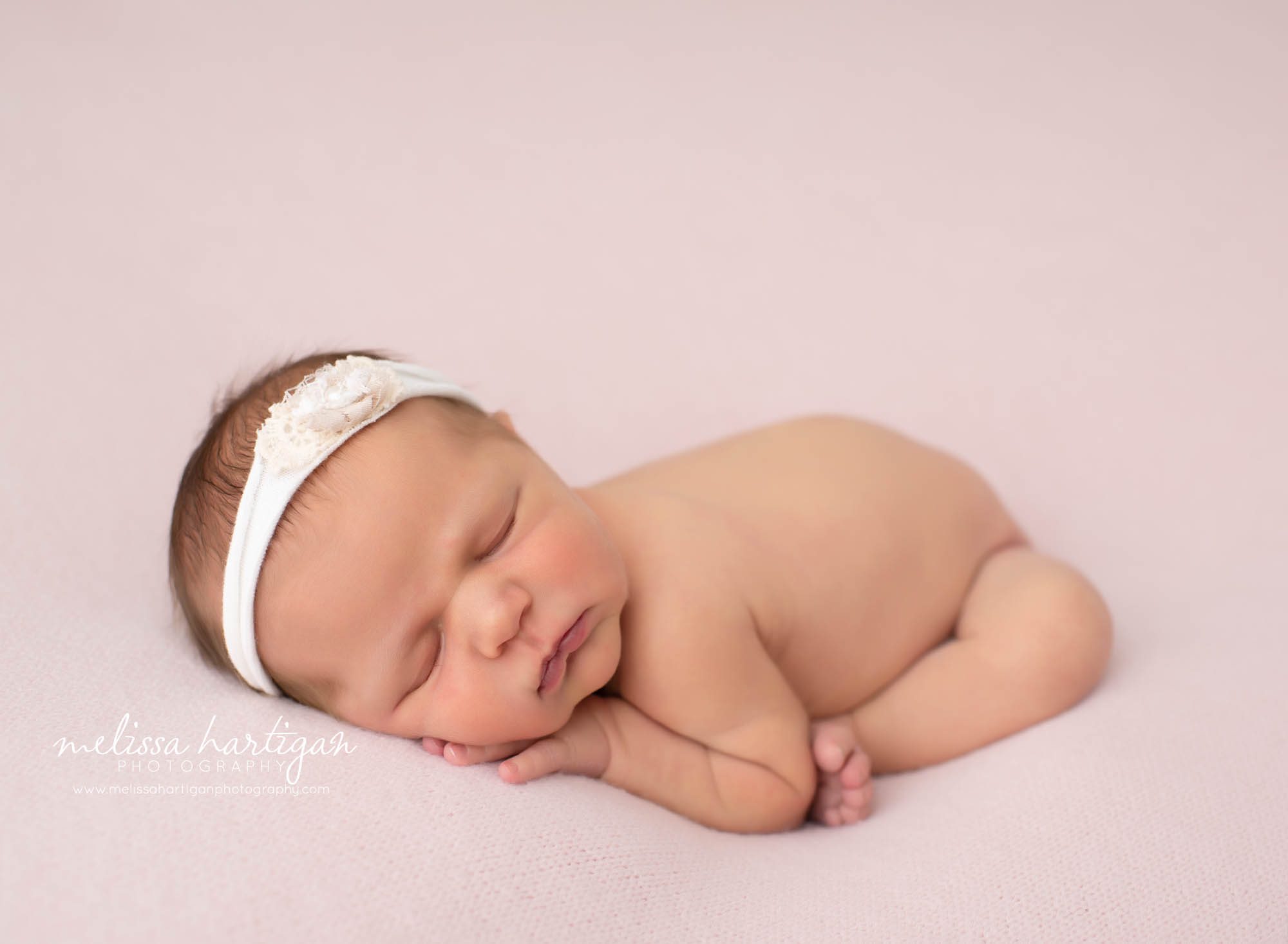newborn baby girl posed on tummy on pink backdrop with white headband
