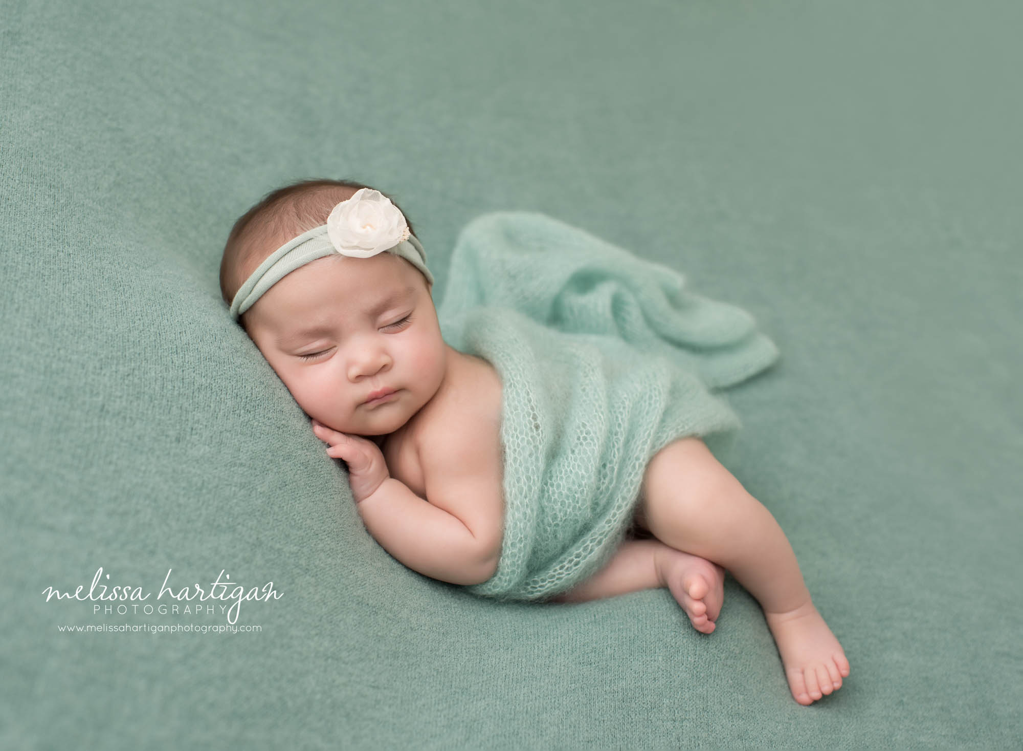 newborn baby girl posed on side tummy with teal green colored flower headband and knitted teal wrap Windsor CT newborn Photography