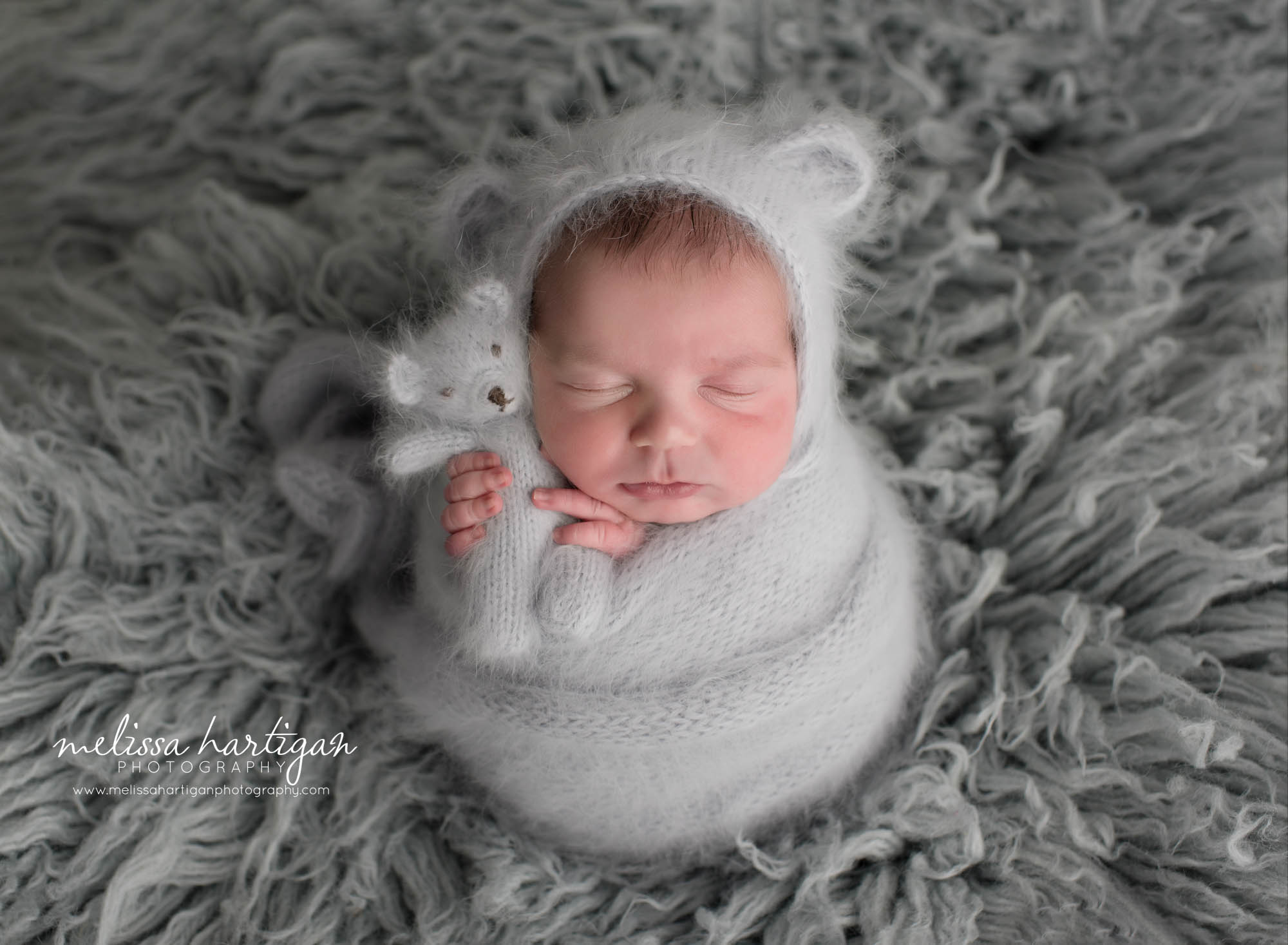 Newborn boy wrapped in gray knitted wrap with matching bear bonnet and teddy