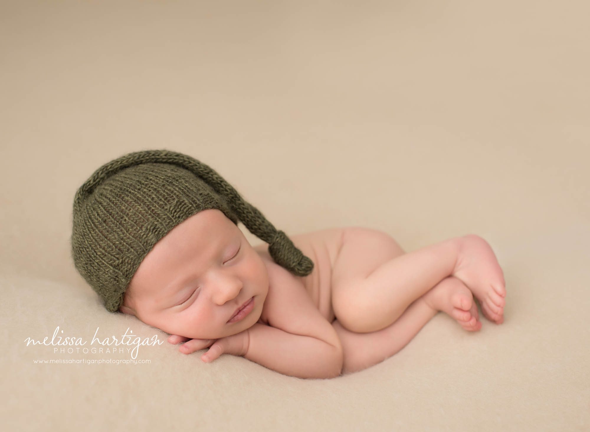 Nebworn baby boy posed on side with knitted green sleepy cap