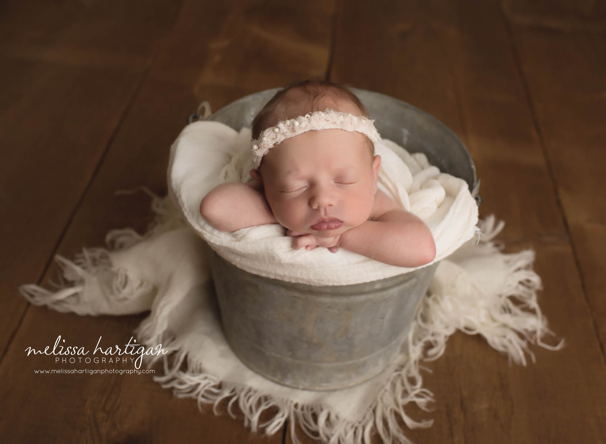 sleeping baby girl posed in metal bucket with cream lay and cream colored headband