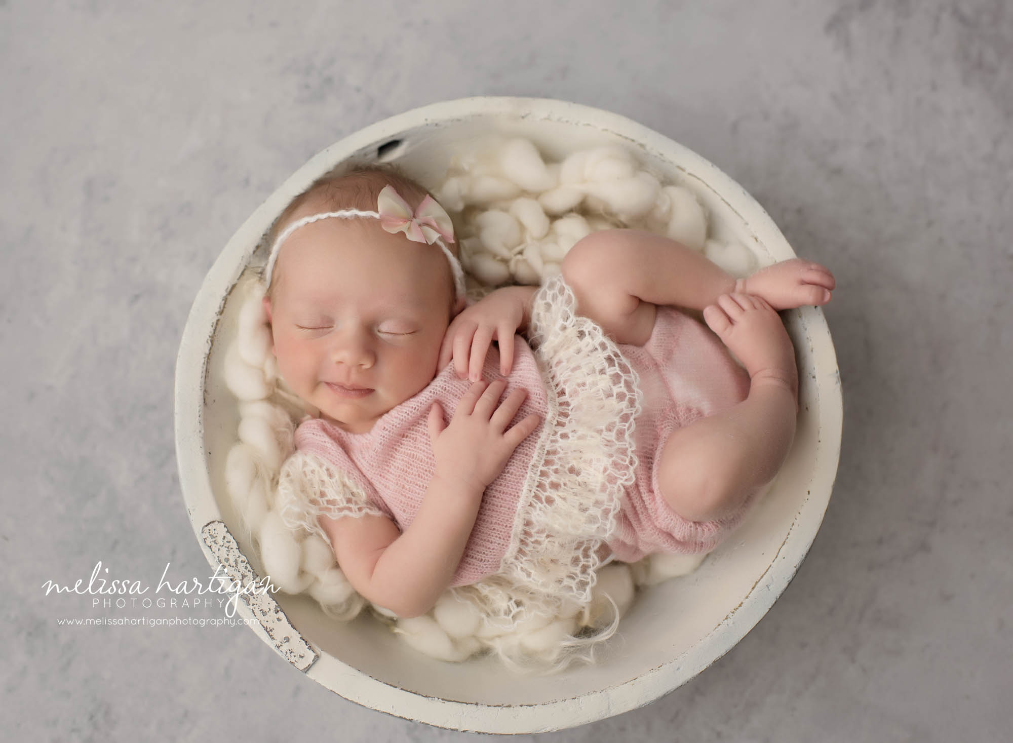 newborn baby girl wearing knitted light pink and cream knitted outfit with pink bow headband sleeping smiling hartford county newborn photography