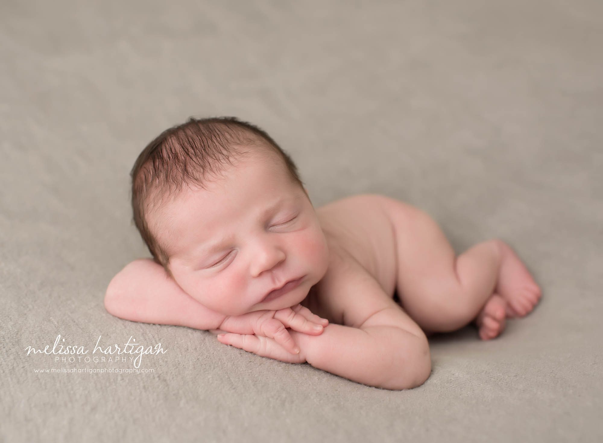 newborn baby boy posed on tummy with head rested on hands