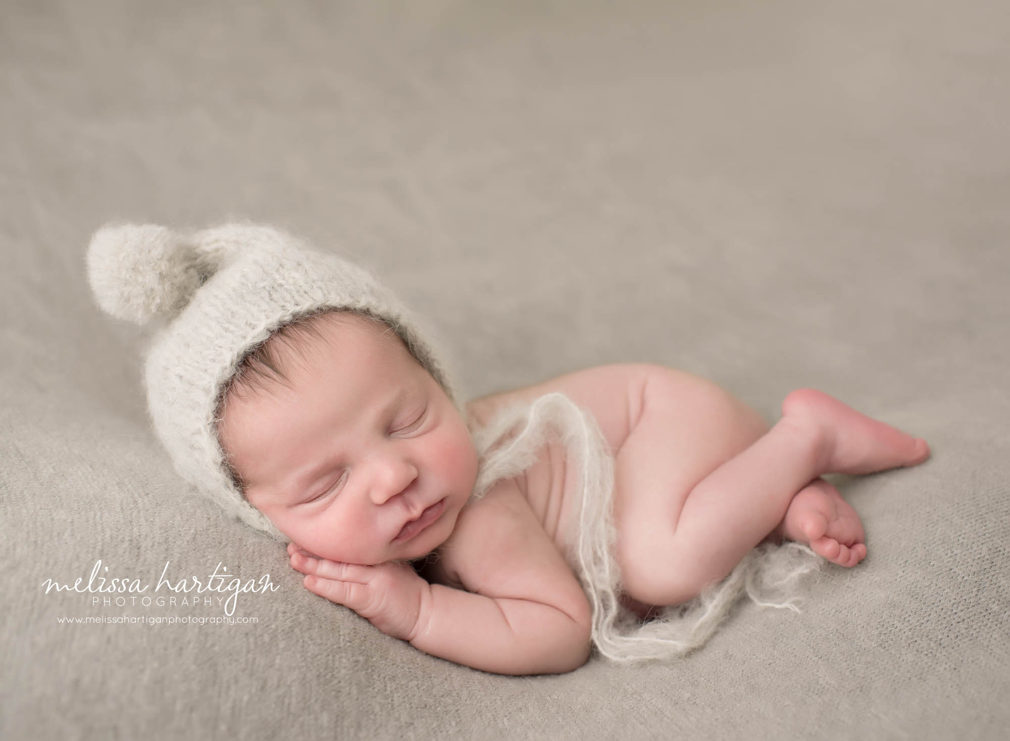Newborn baby boy posed on side with pom newborn bonnet hat