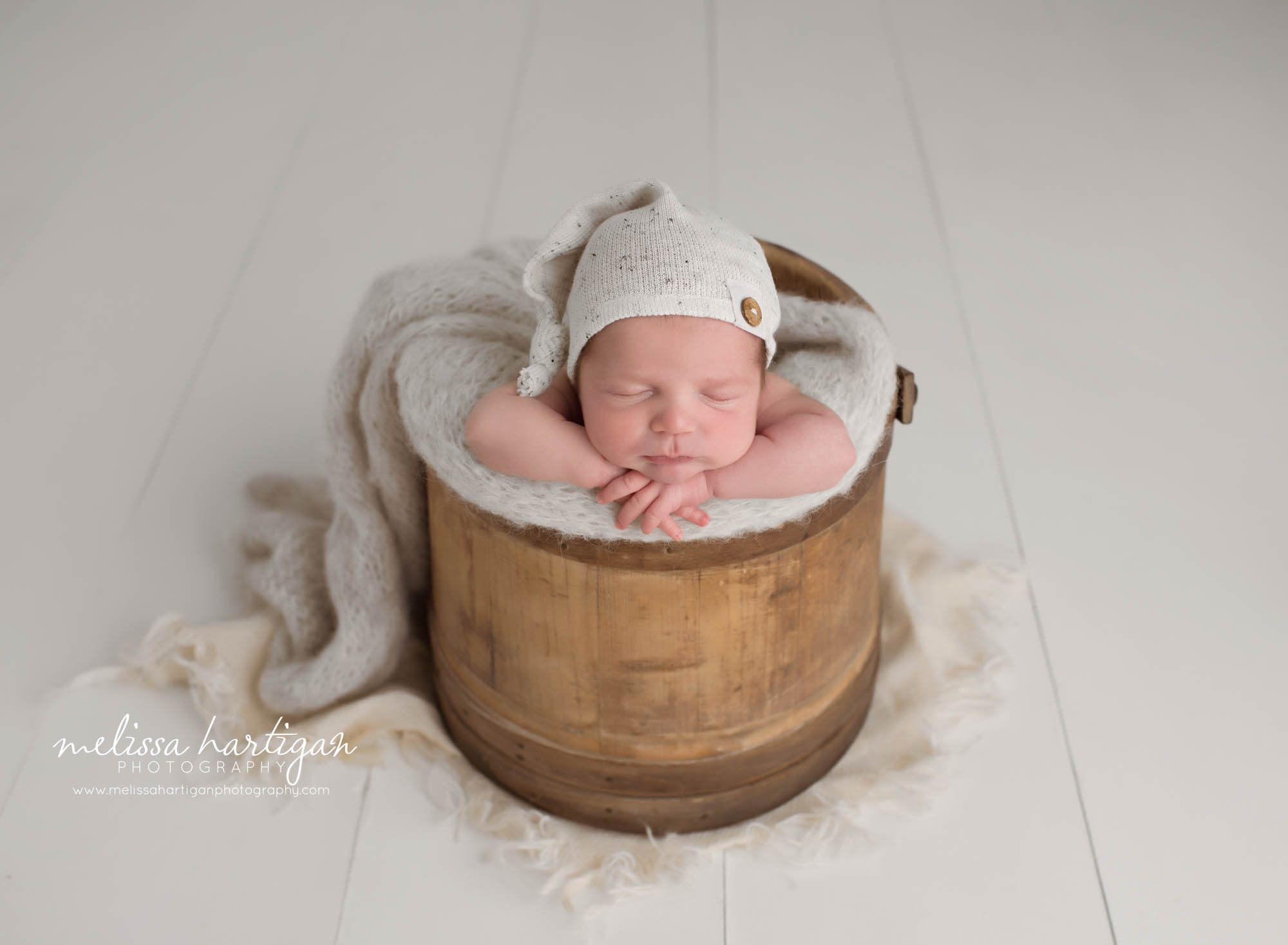 newborn baby boy posed in wooden barrel bucket with light gray knitted wrap and cream colored sleep cap bonnet MA newborn photography CT
