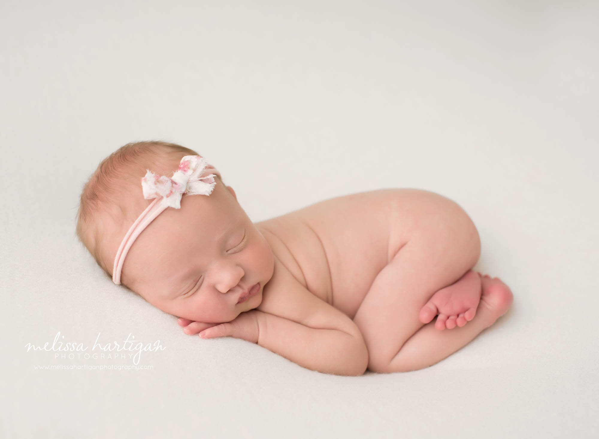 newborn baby girl posed on tummy with pink bow headband