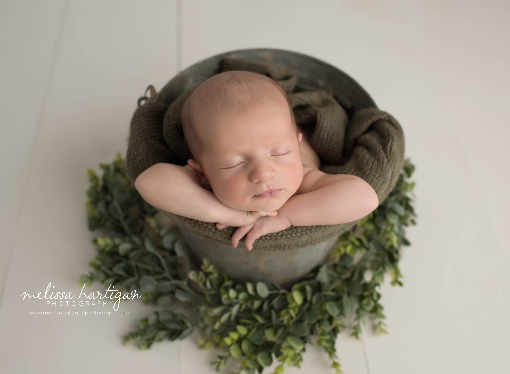 newborn baby boy posed in bucket with green knitted wrap and green foliage tolland county baby photography