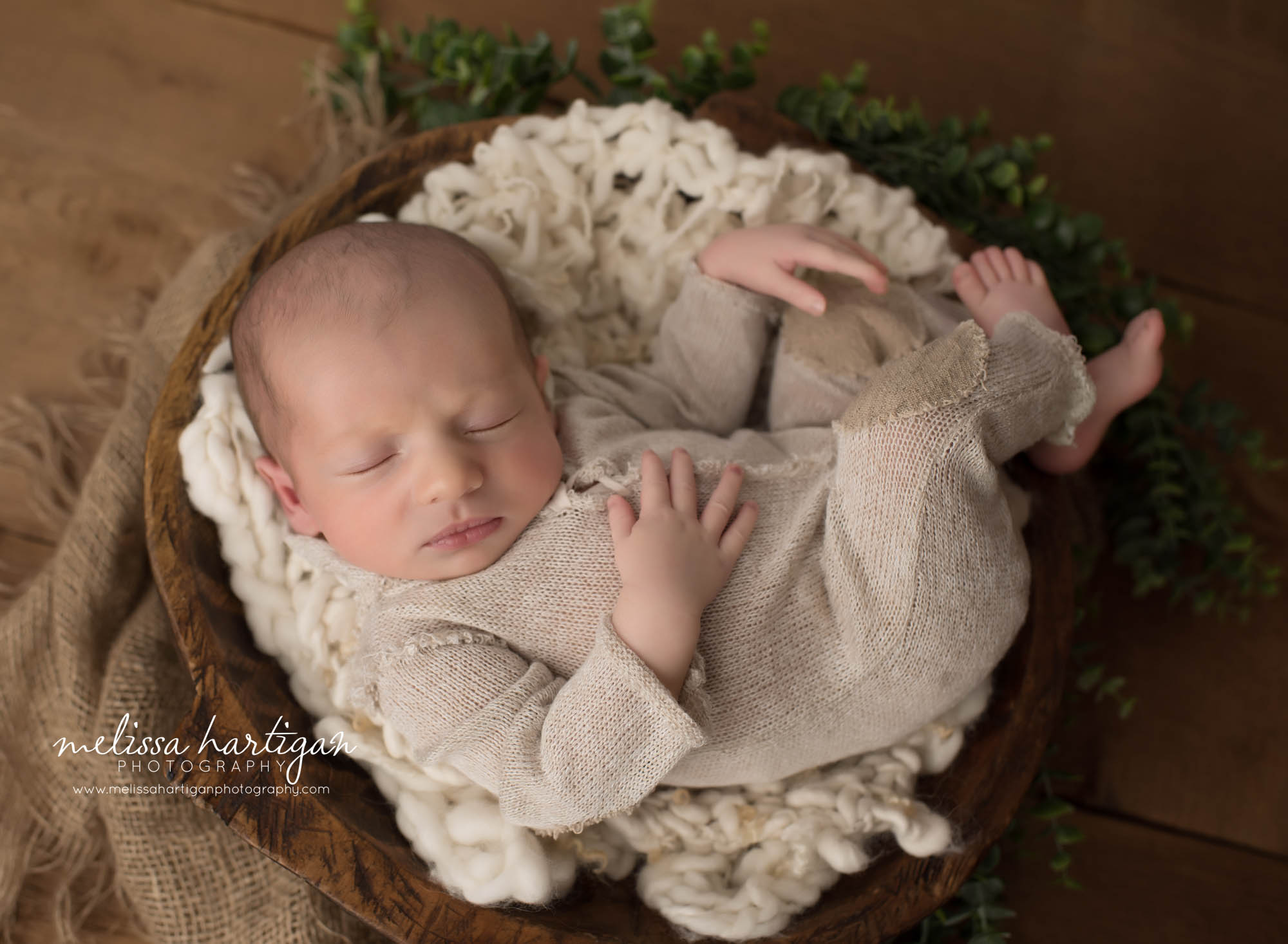 newborn baby boy wearing knitted outfit posed in wooden bowl