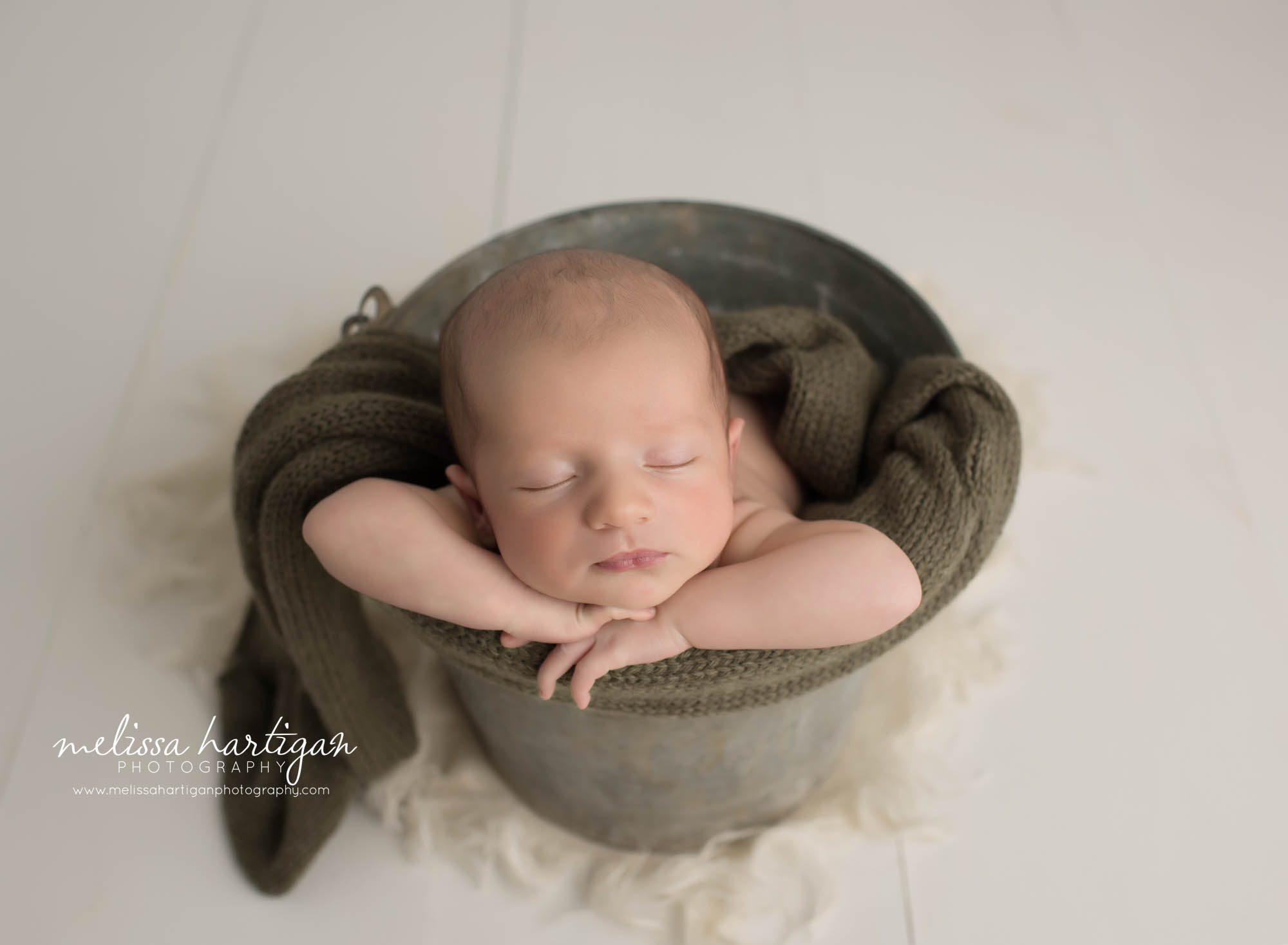 newborn baby boy posed in metal bucket with green knitted wrap layer