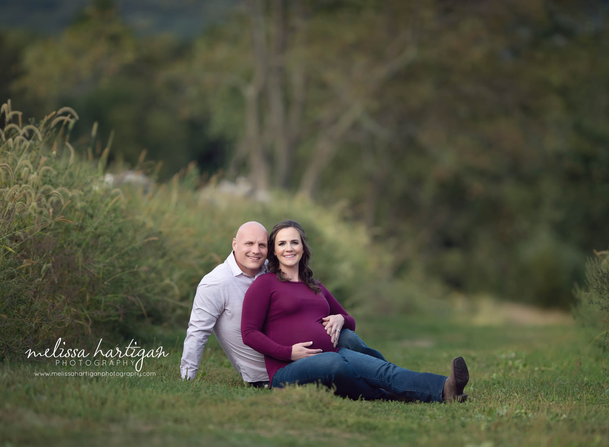 mom and dad to be sitting on grass holding baby bump CT maternity Newborn Photographers