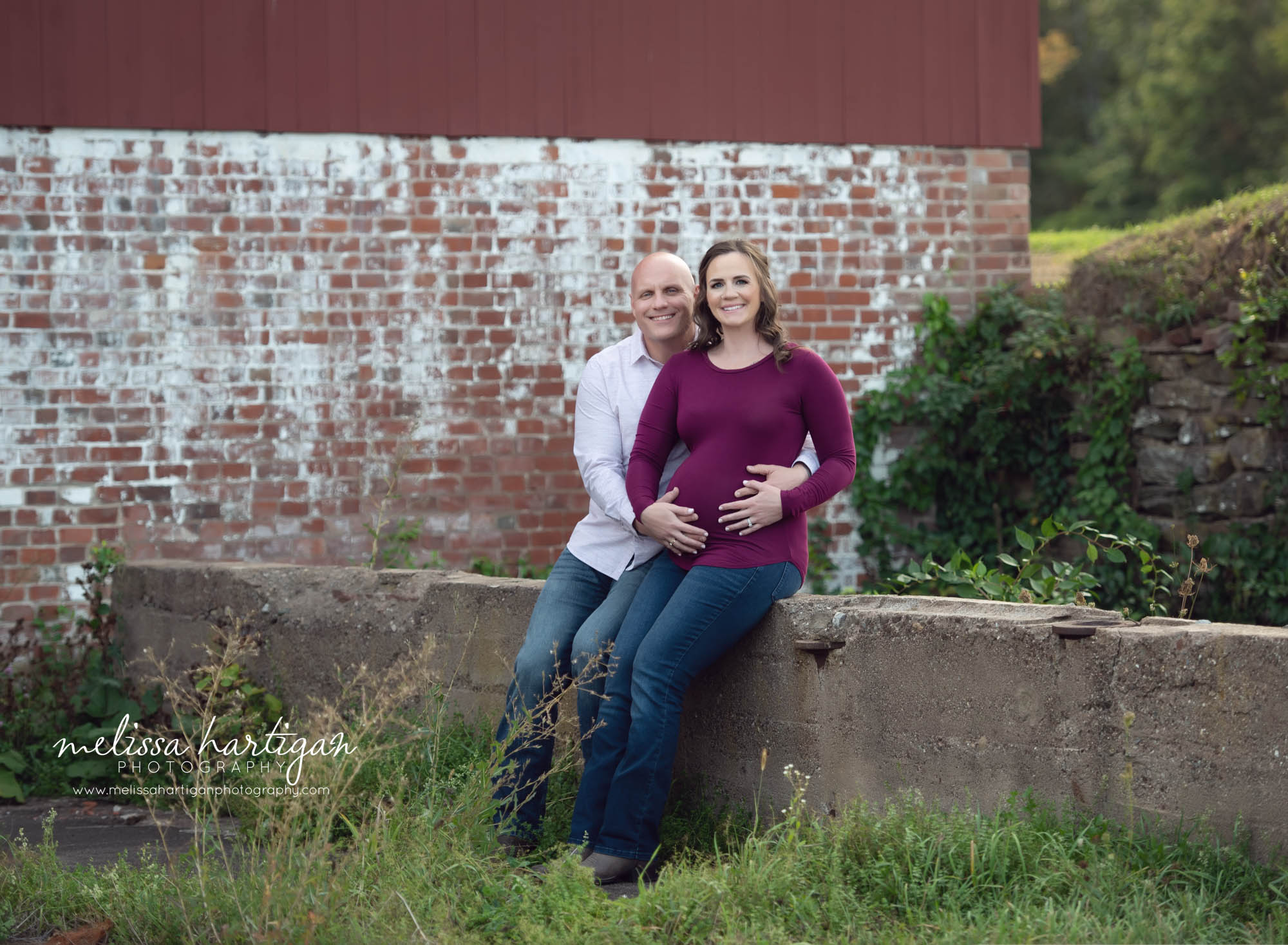pregnant mom and dad to be sitting on stone wall holding baby bump maternity photography CT