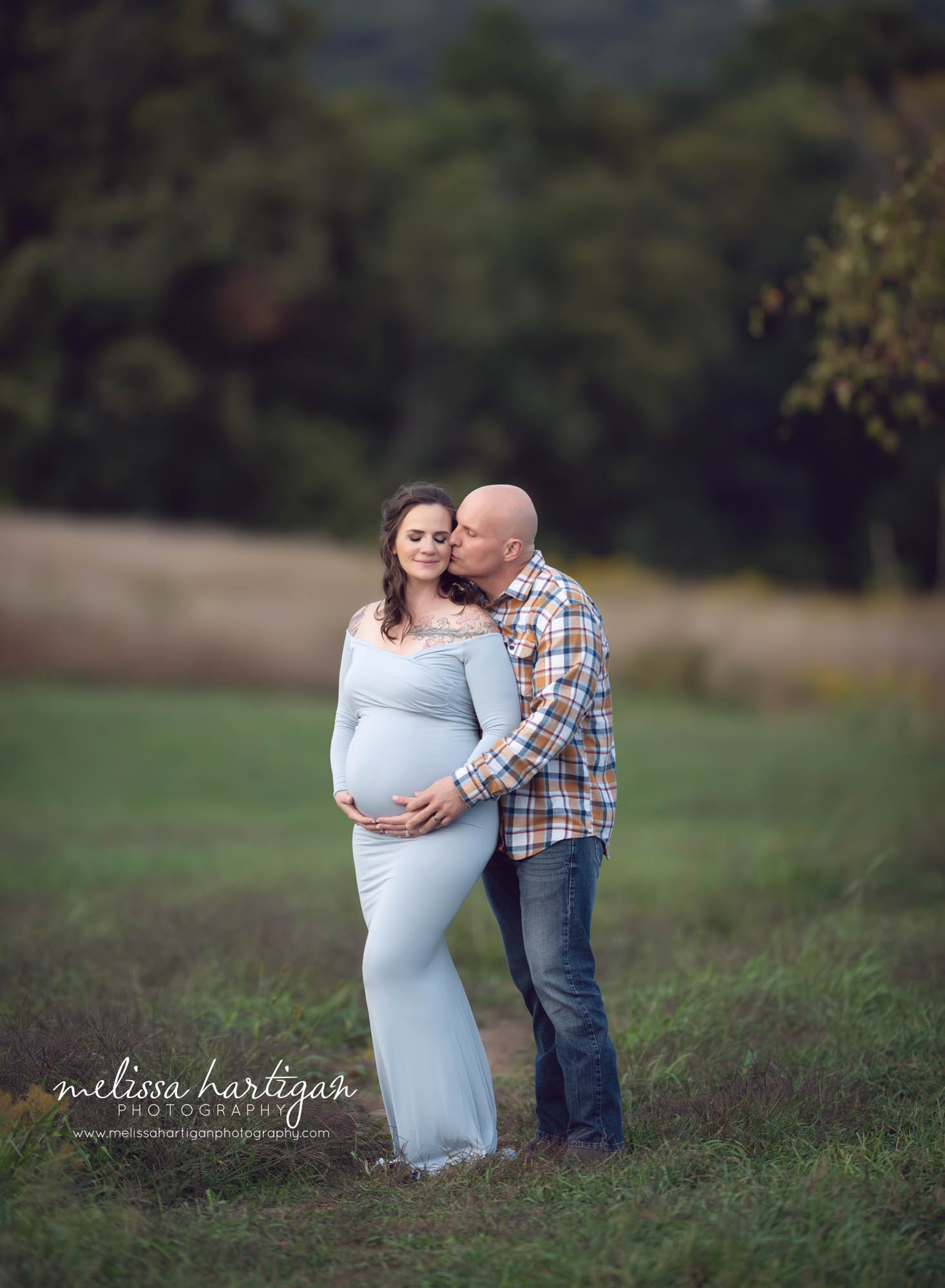 dad kissing pregnant mom to be on side of cheek holding baby bump CT maternity photographer