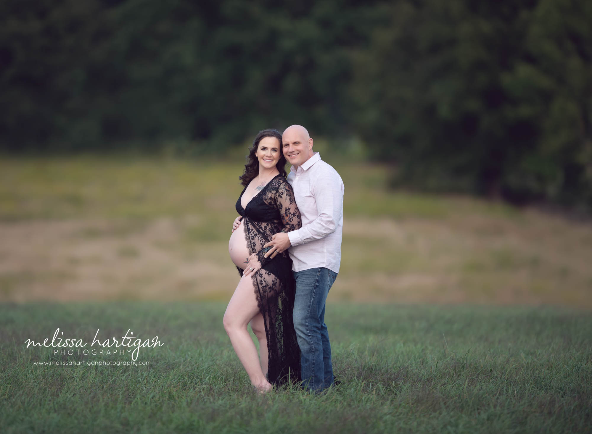 mom to be wearing black lace open front maternity robe smiling dad to be behind her holding her arm smiling happy couple CT maternity newborn photography