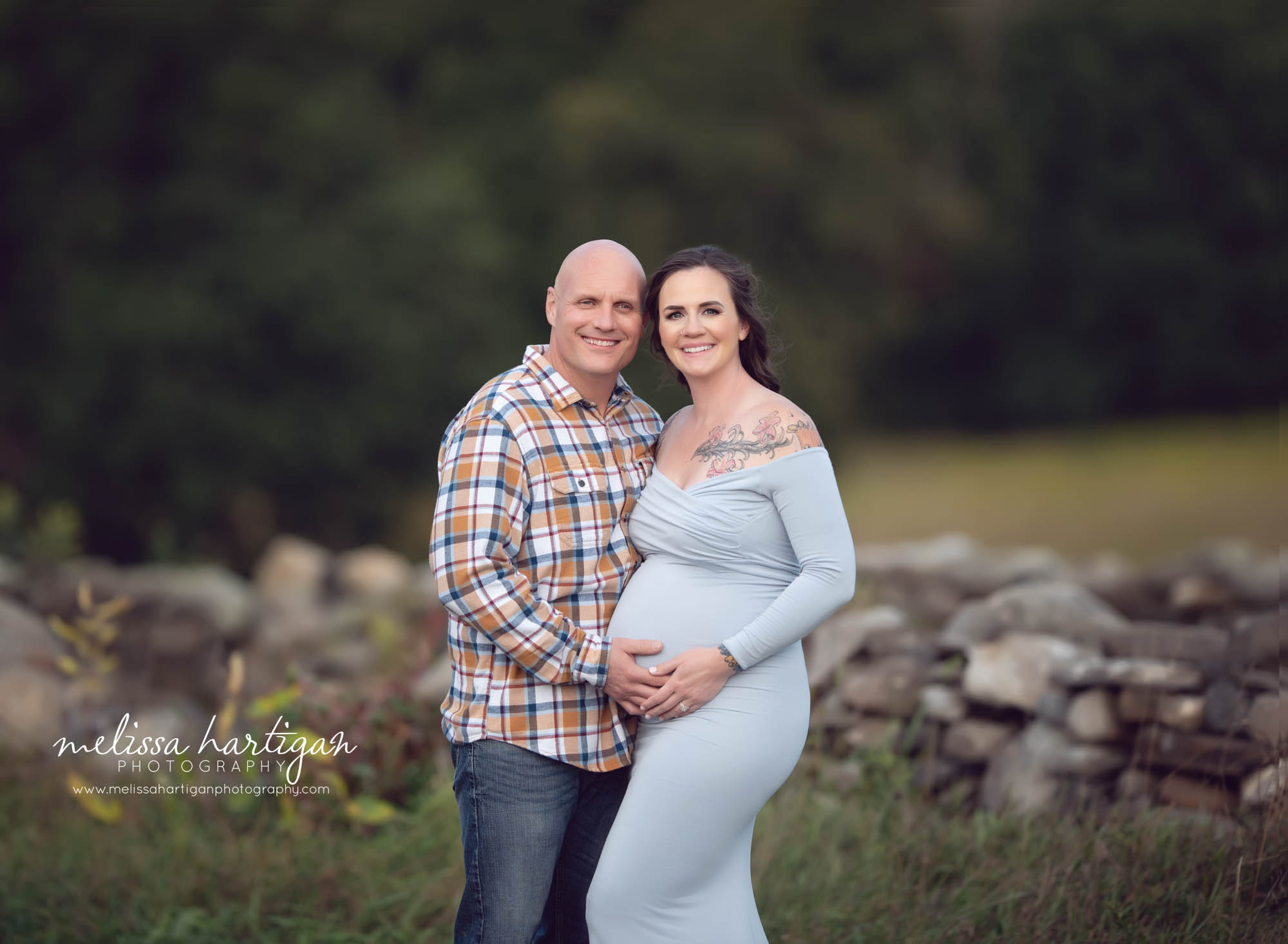smiling couple happy excited pregnant mom wearing light blue long form fitted dress holding baby bump