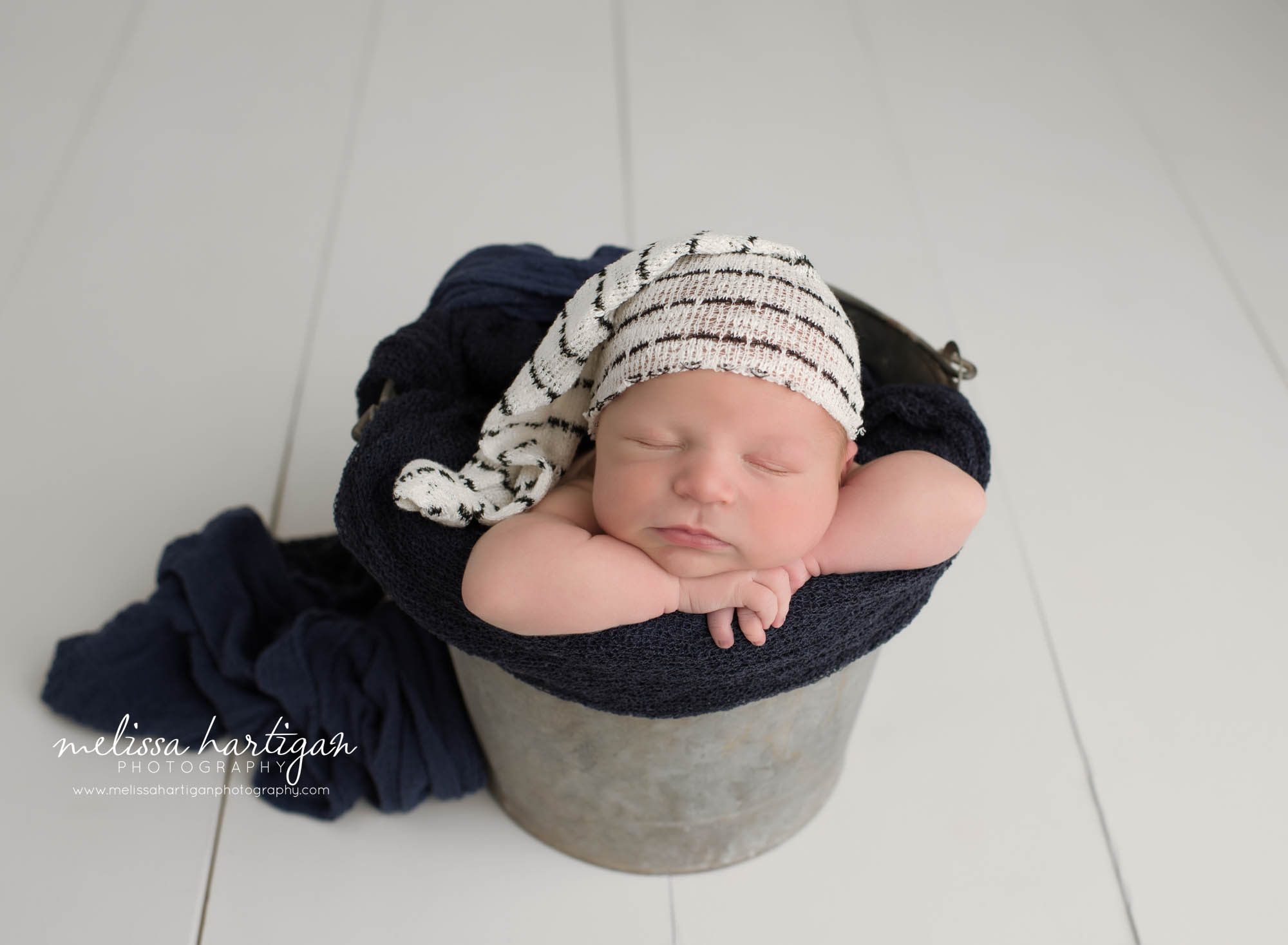 newborn baby boy posed in bucket with navy blue wrap and white and navy striped sleepy cap CT newborn Photography