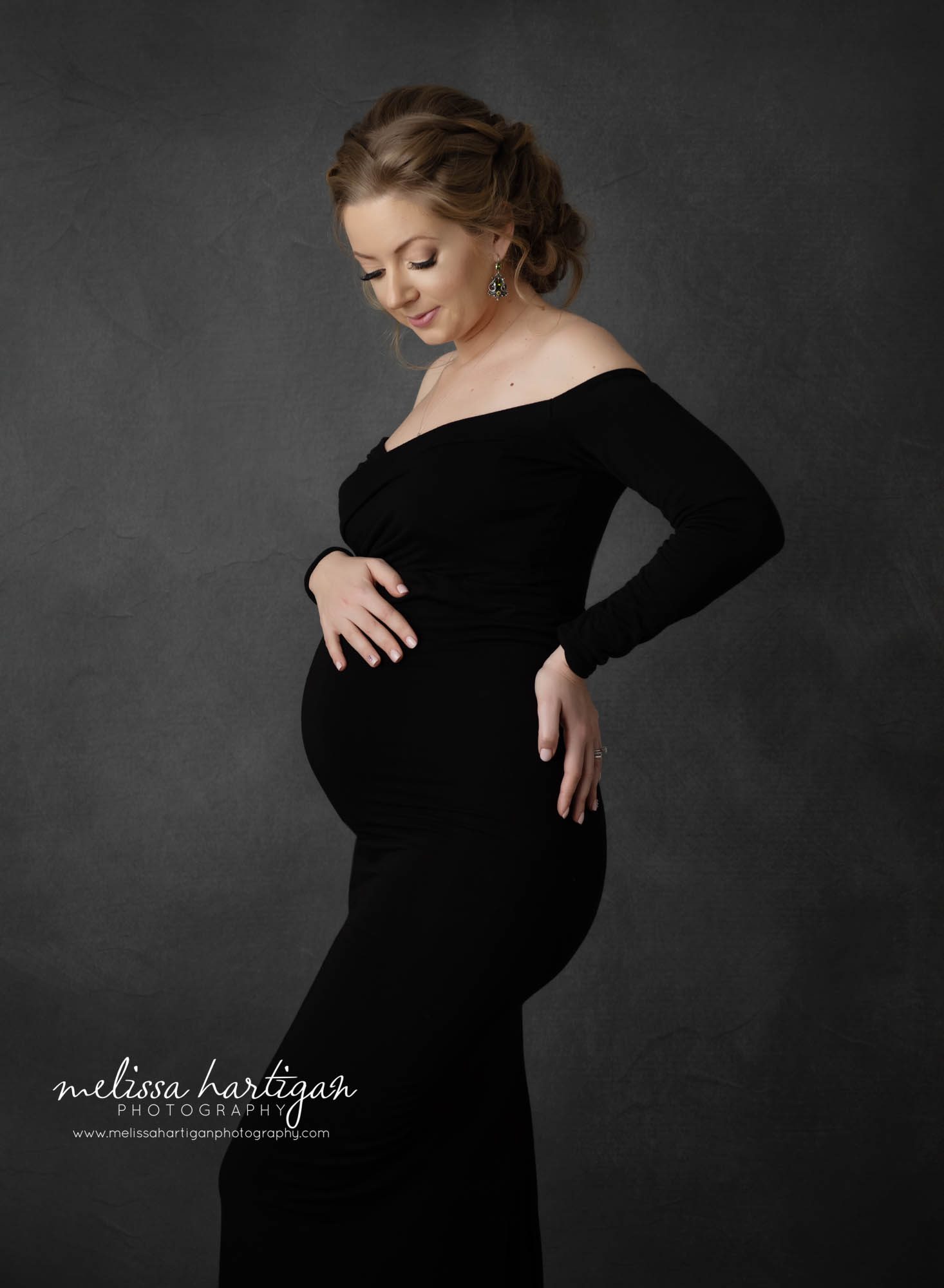 Pregnant mom standing maternity photography pose holding baby bump looking down at belly
