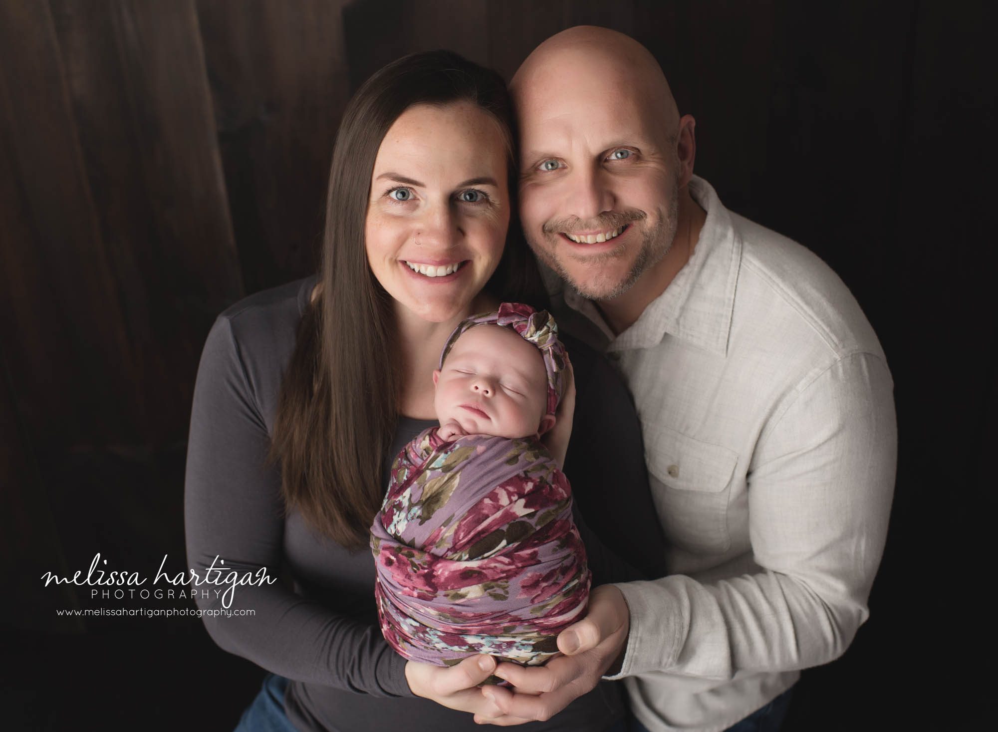 mom dad holding newborn baby daughter wrapped in floral wrap and matching floral headband newborn family photographer CT