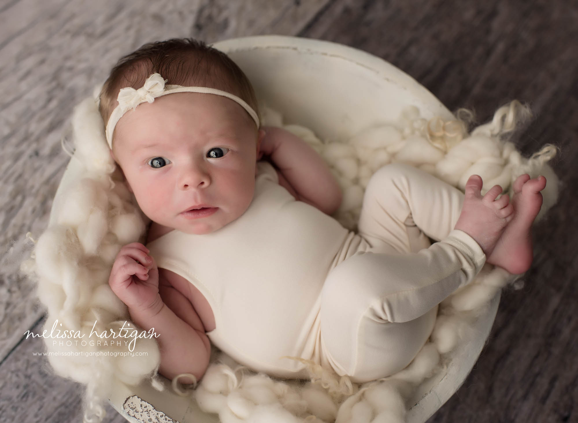 awake newborn baby girl wearing cream romper with bow tie back posed in creamo wooden bowl with braided cream layer