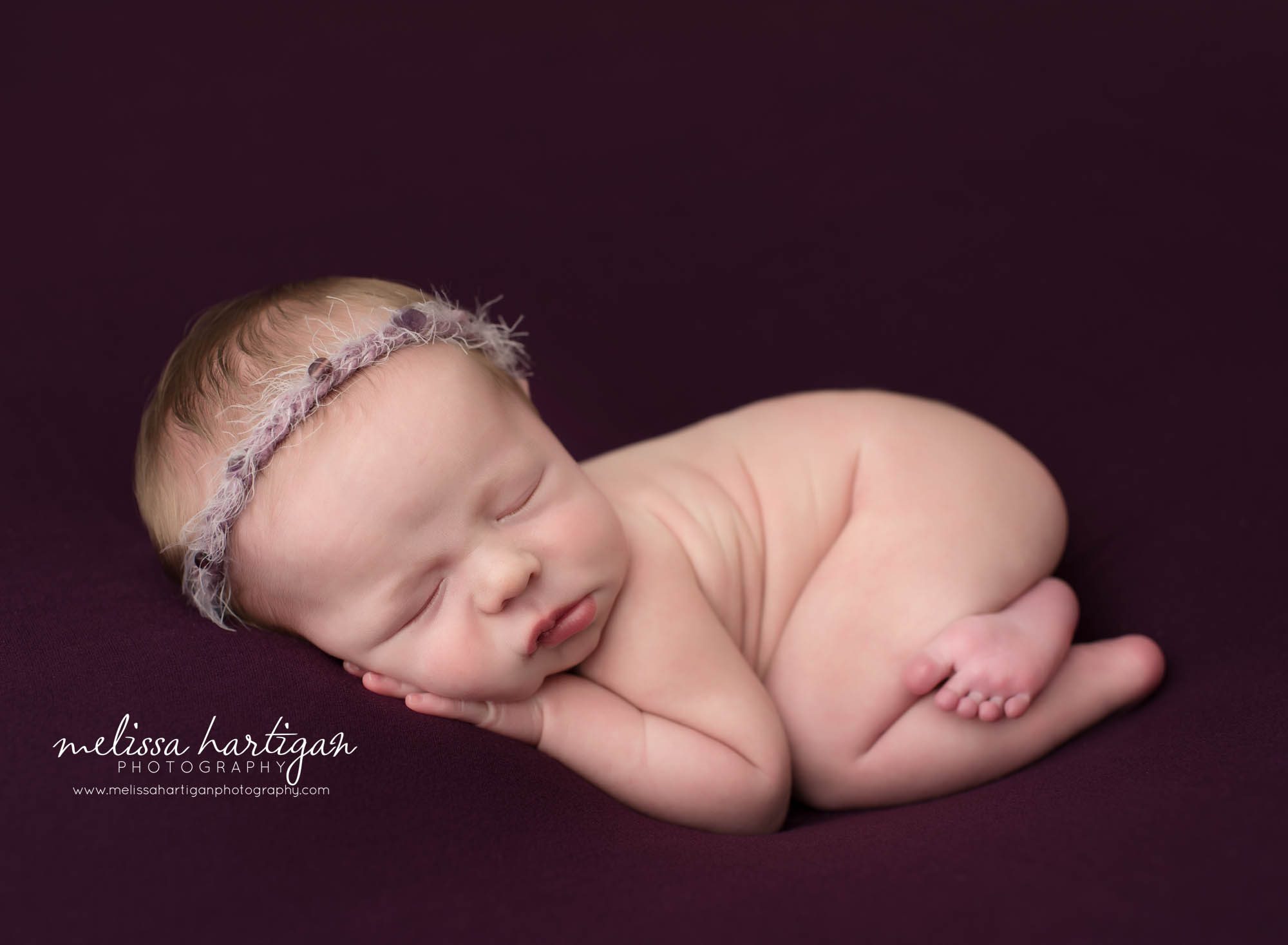newborn baby girl posed on tummy with purple tie back