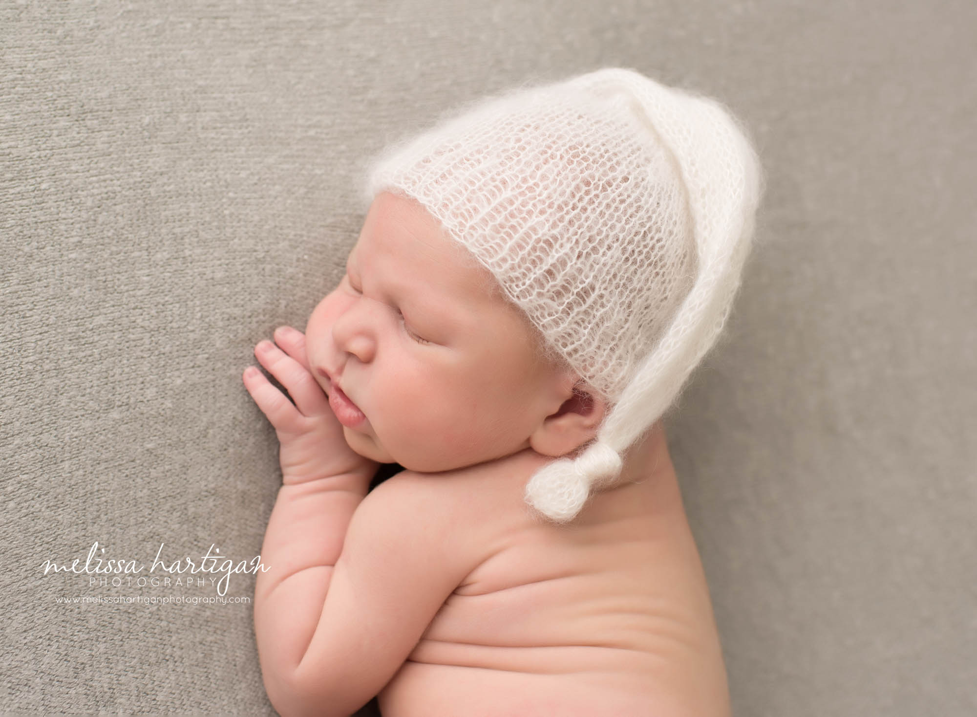 newborn baby boy posed on side with white cream knitted newborn sleepy cap [posed on gray backdrop norwalk newborn photographer
