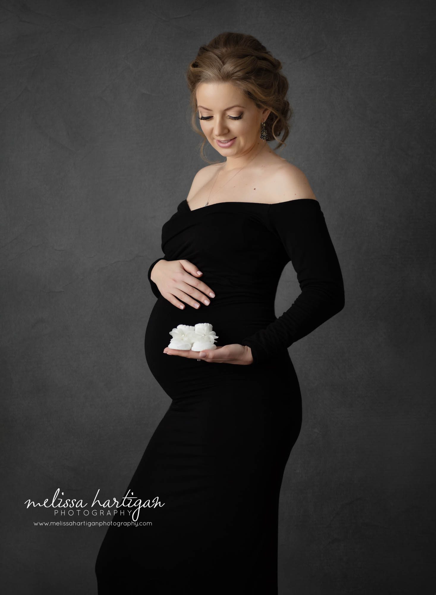 pregnant mom holding baby shoes looking down at belly