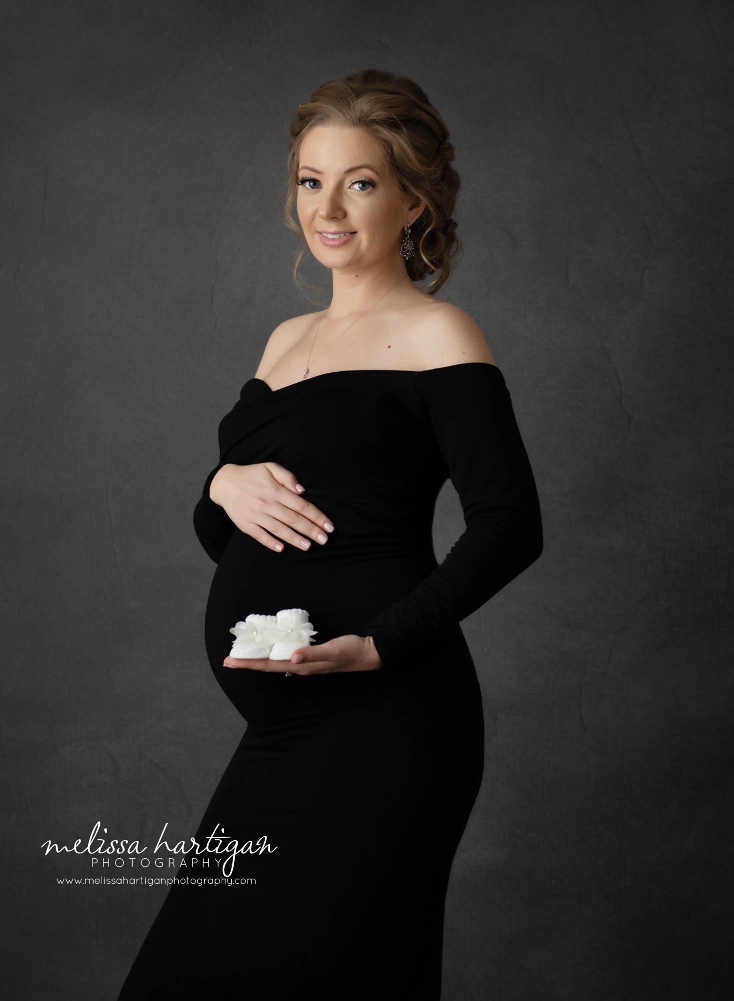 mom to be holding white baby shoes pregnancy photoshoot