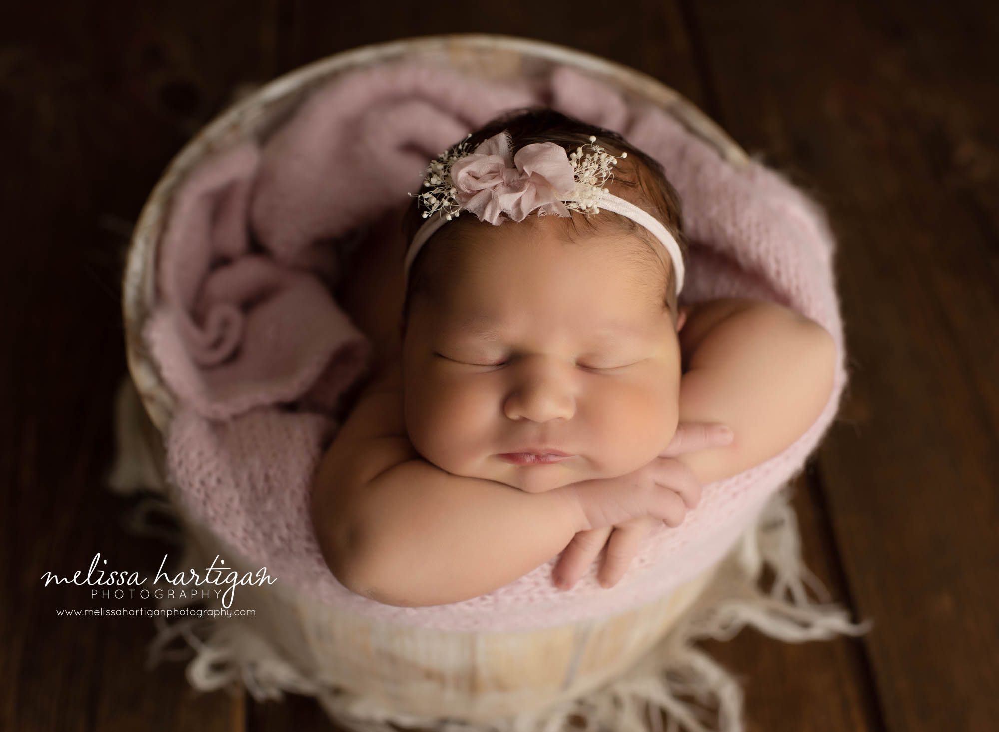 newborn baby girl posed in wooden bucket with pink layer wrap and flower headband