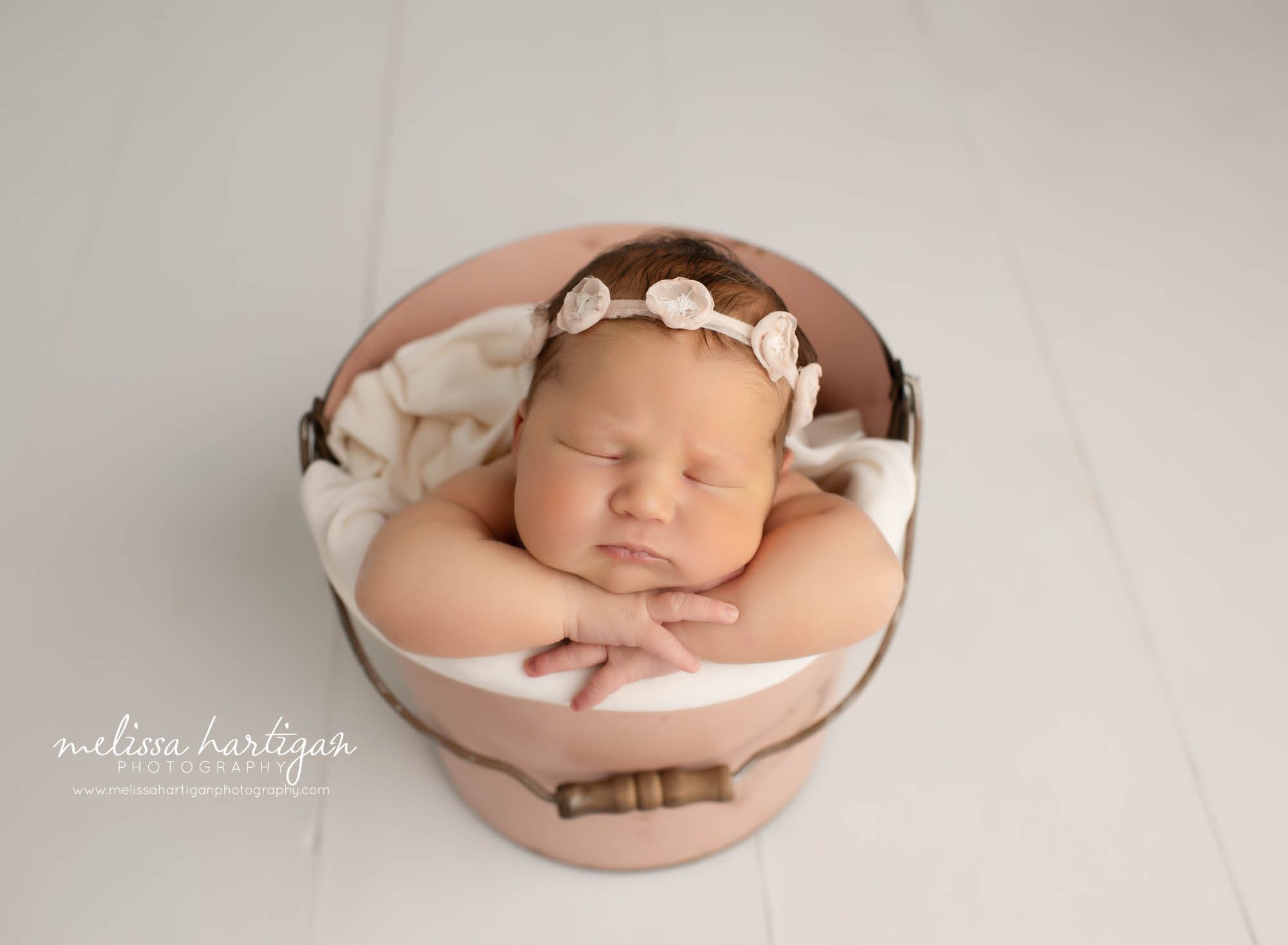 newborn baby girl posed in bucket with flower headband