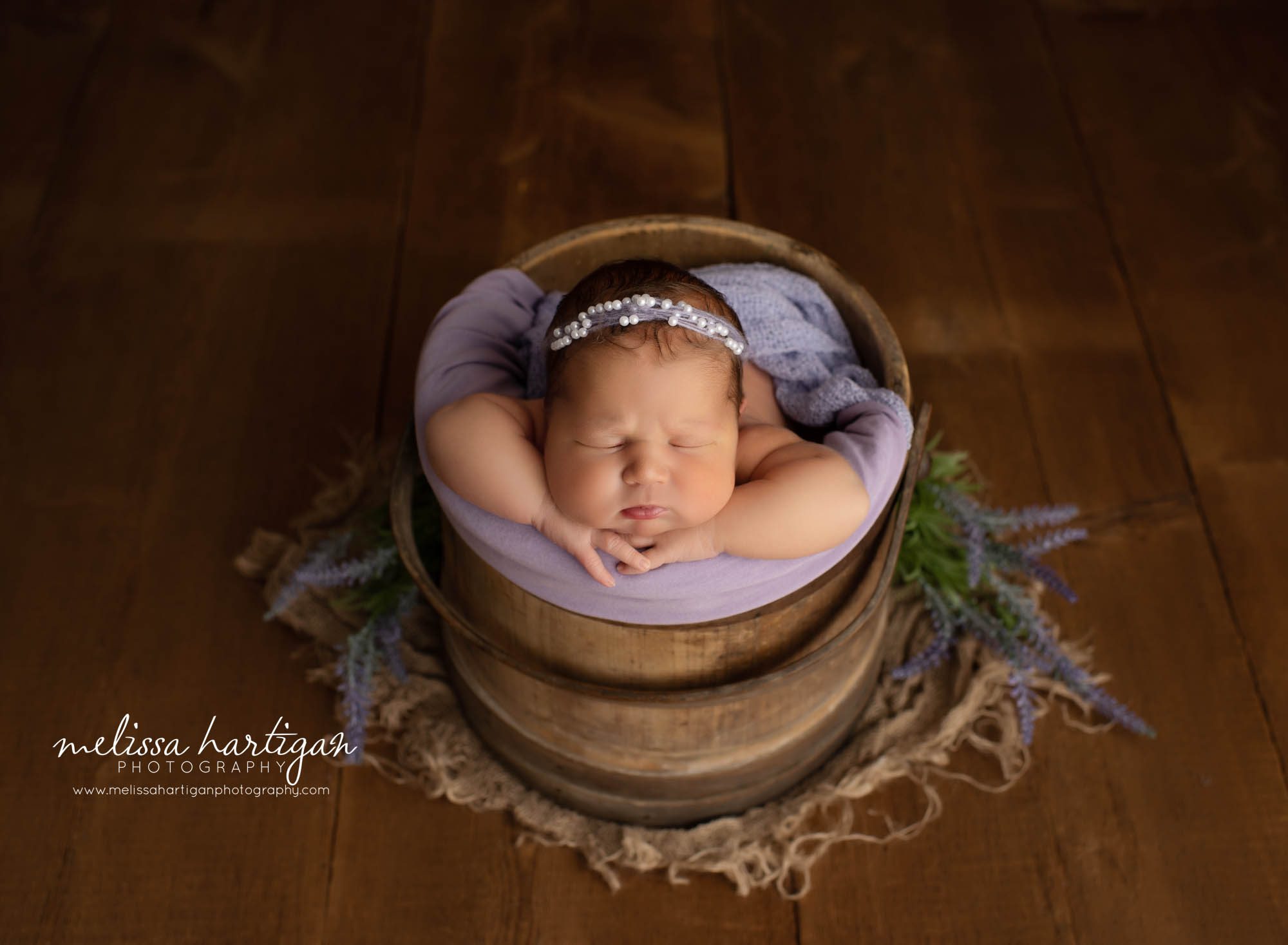 newborn baby girl posed in wooden bucket with purple lavendar stems