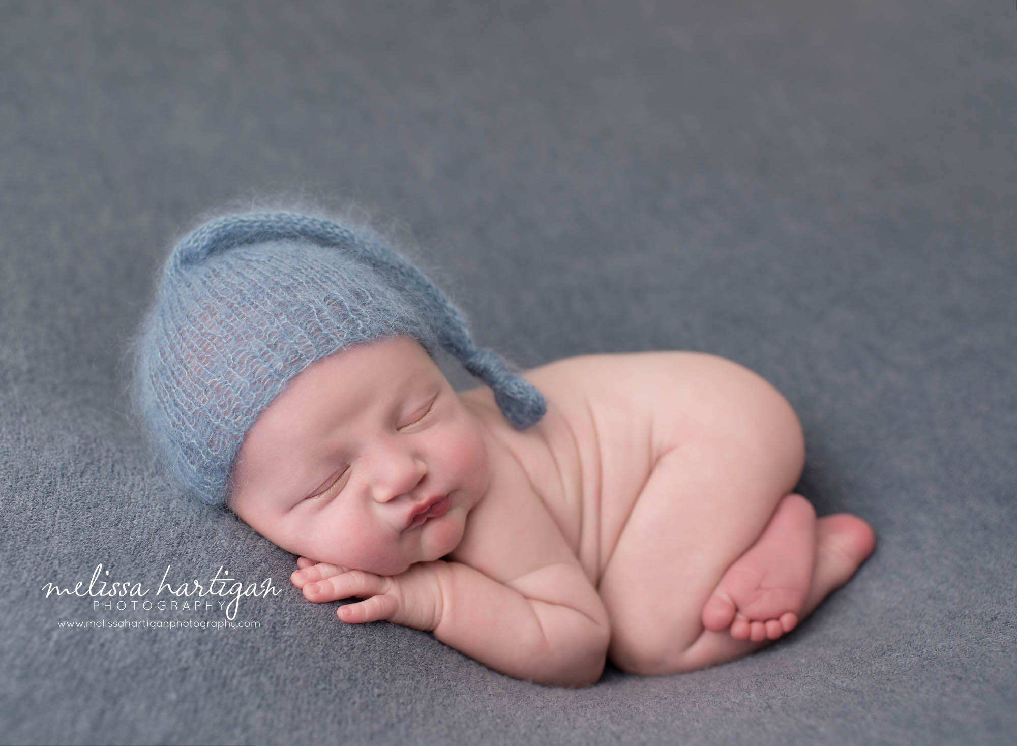 sleeping newborn baby boy posed on tummy with hand under cheek wearing knitted blue sleepy cap