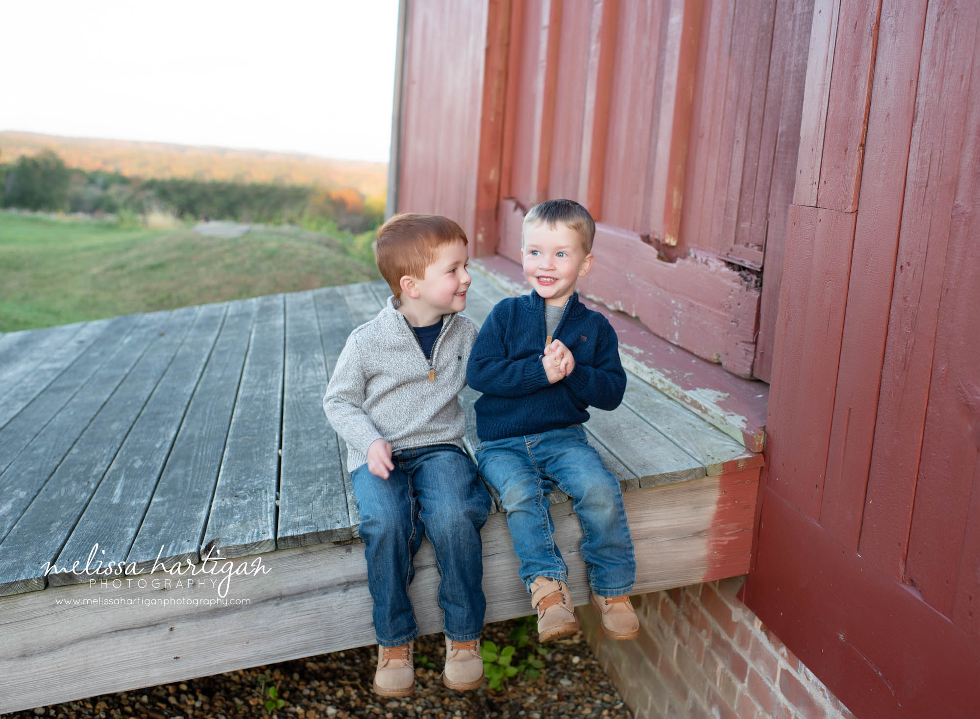 sibling brothers sitting on wooden ramp on farm house