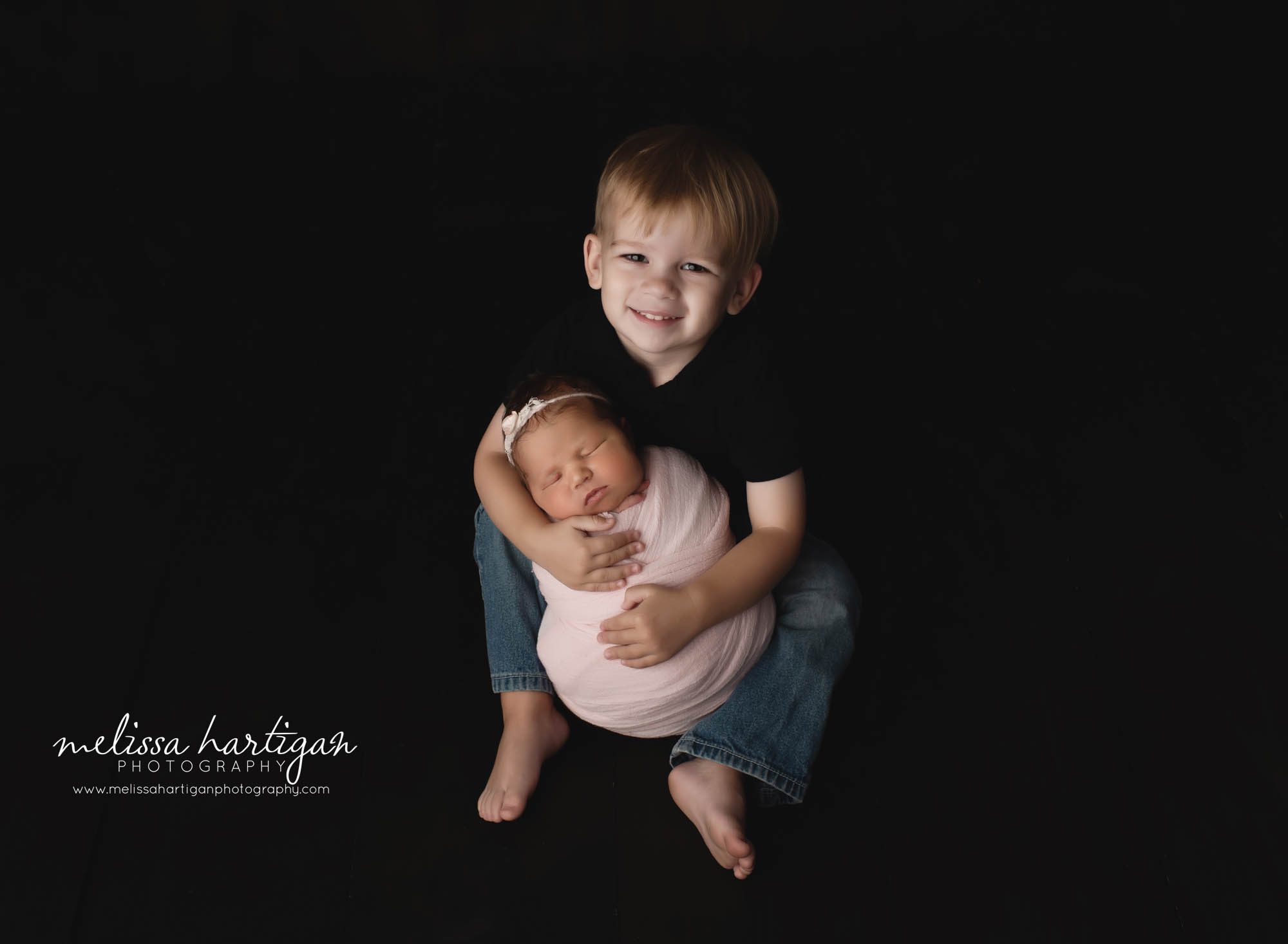 big brother holding wrapped newborn baby sister