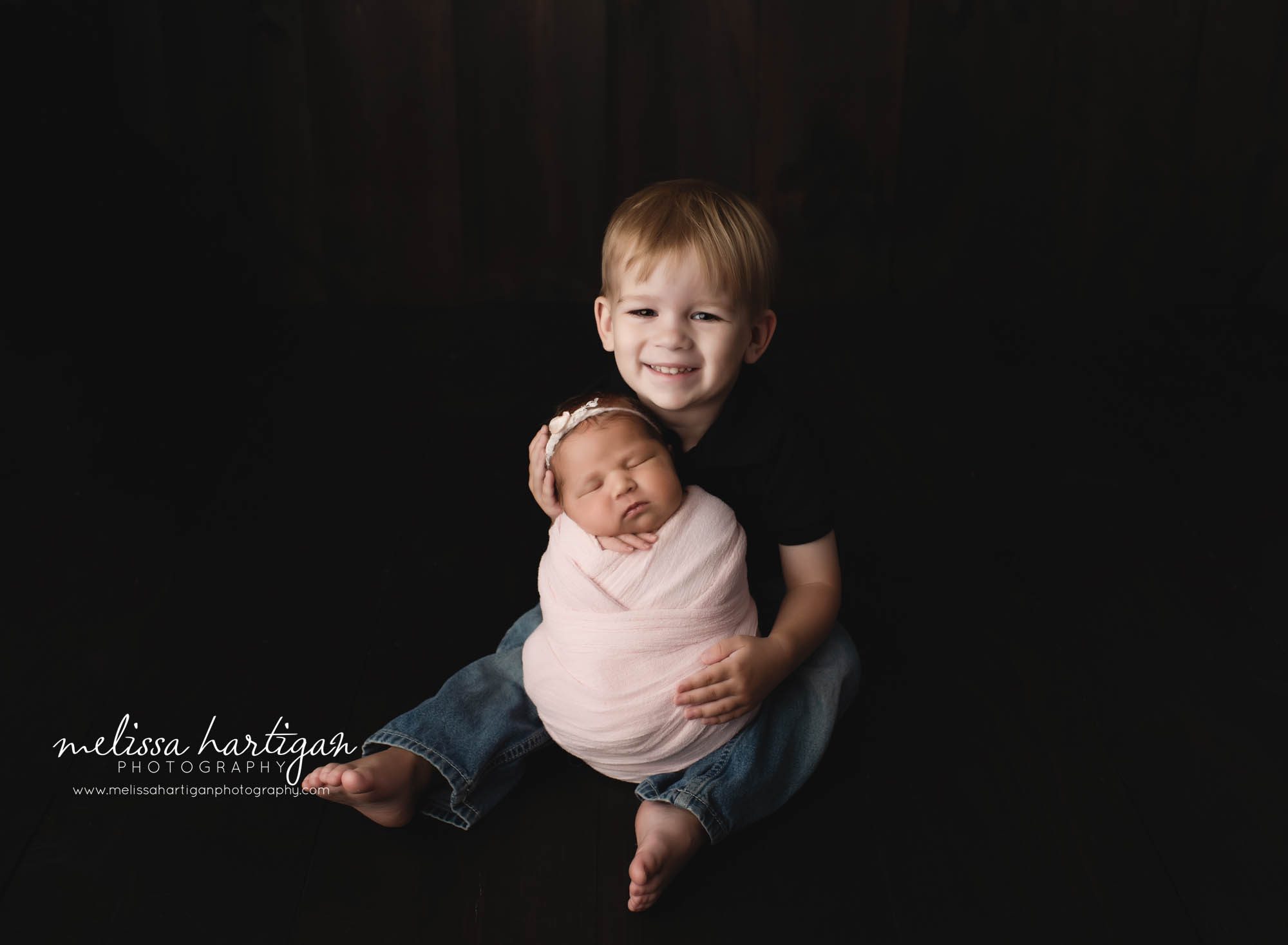 big brother smiling holding wrapped newborn baby sister