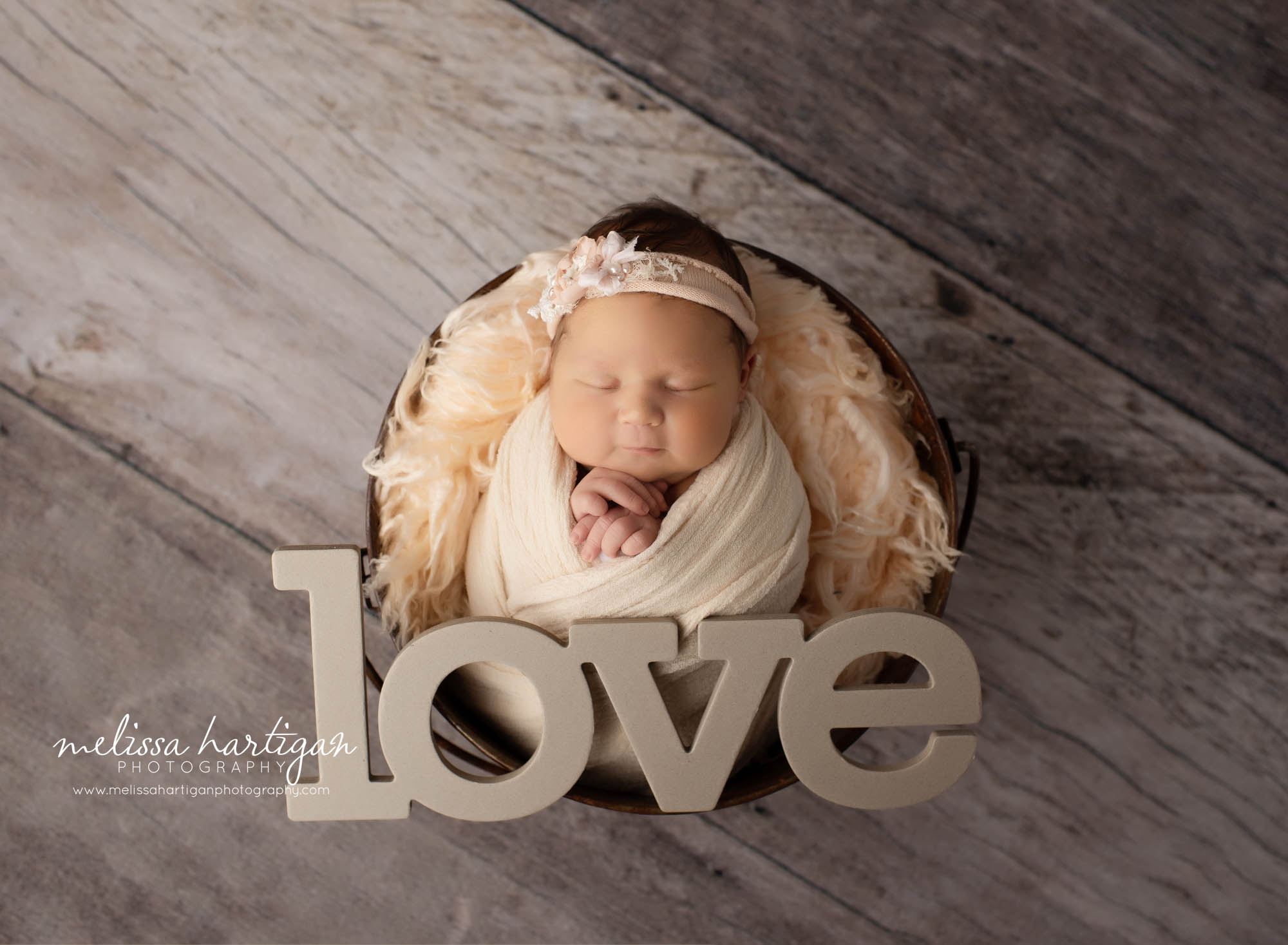 Newborn baby girl wrapped in peach color posed in bucket with love newborn prop