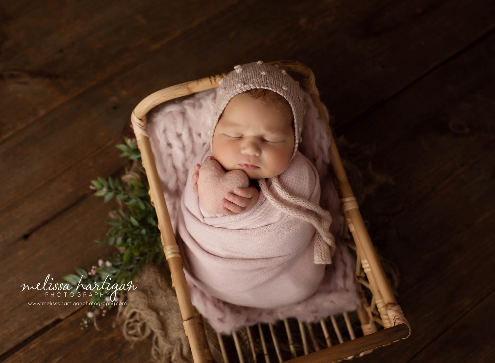 newborn baby girl wrapped in pink posed in basket with pink heart prop