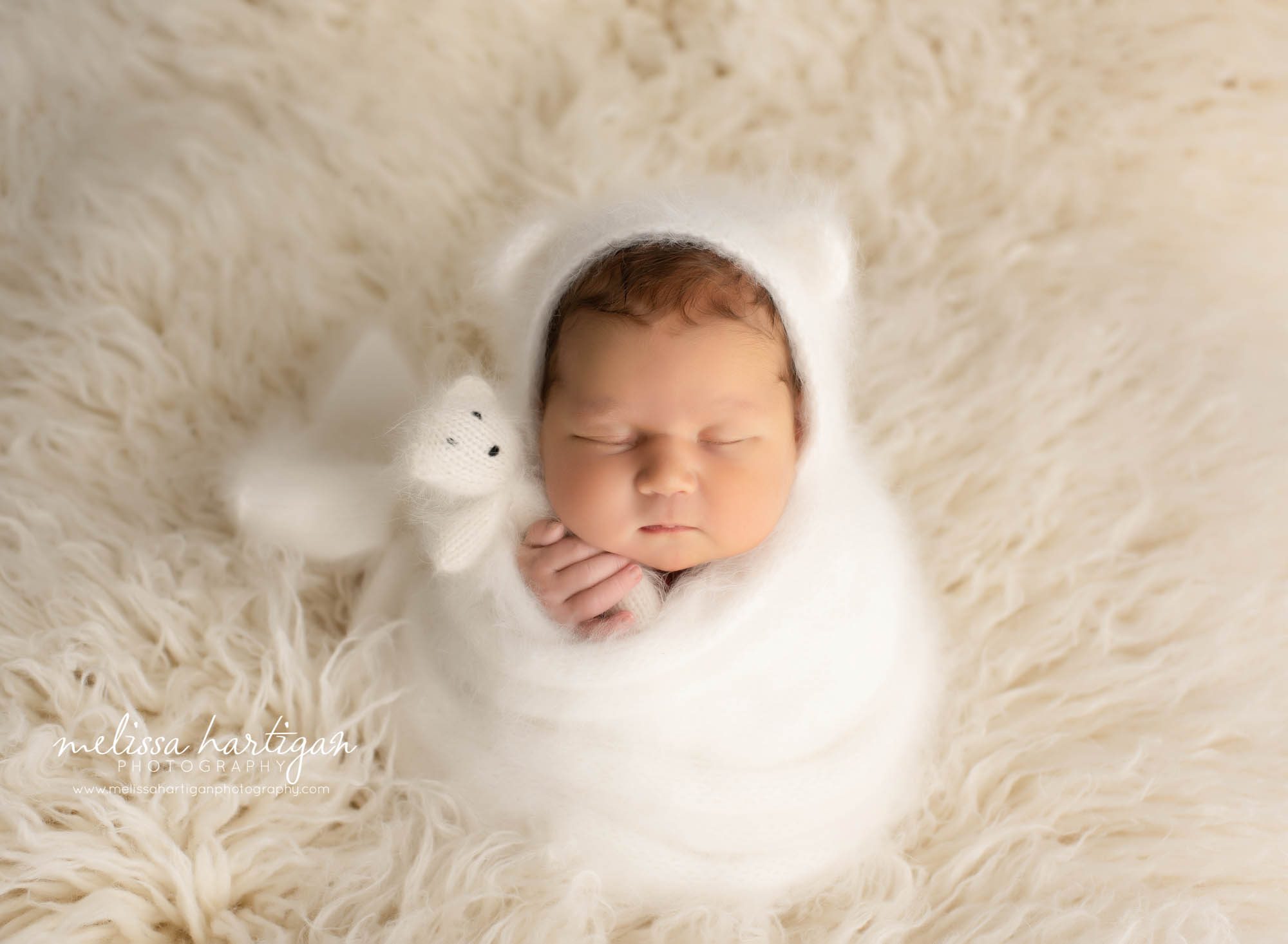 newborn baby girl wrapped in knitted white wraped with matching bear bonnet and teddy bear