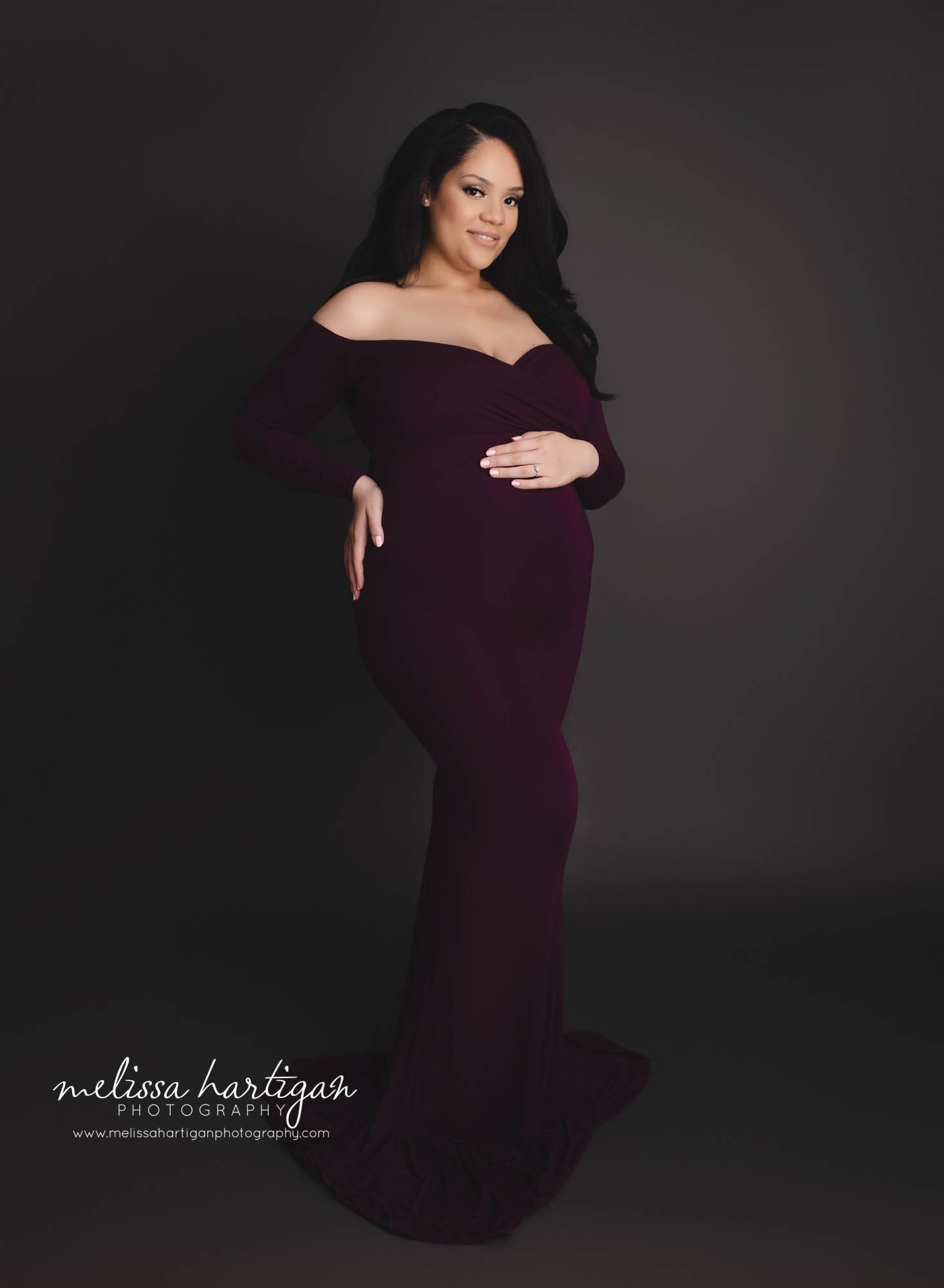 mom holding side and baby bump standing maternity photography pose eggplant purple maternity dress
