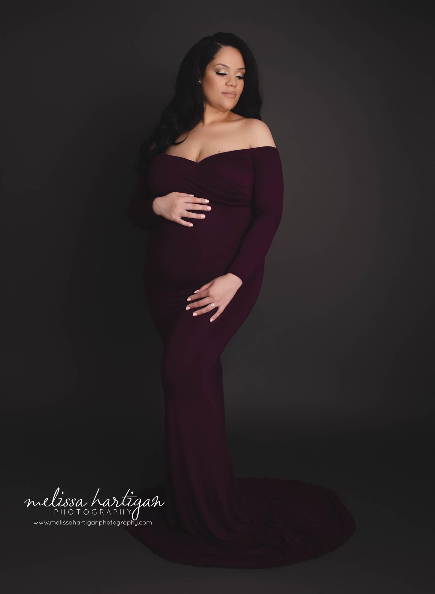 mom looking off to side holding baby bump wearing long for fitted sweetheart neckline eggplant purple maternity gown dress