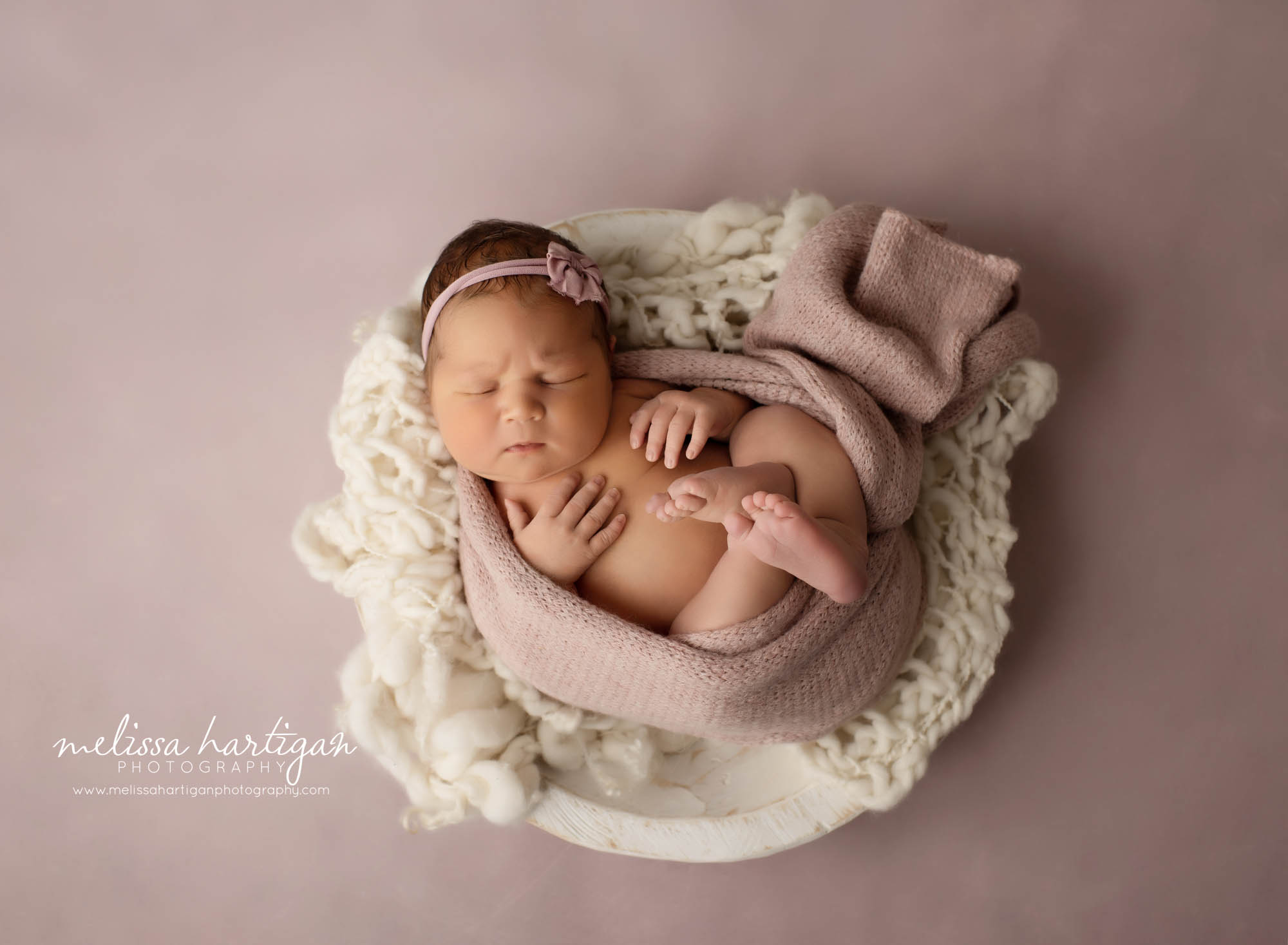 newborn baby girl posed in wooden bowl with pink wrap and pink bow headband hartford county newborn photography
