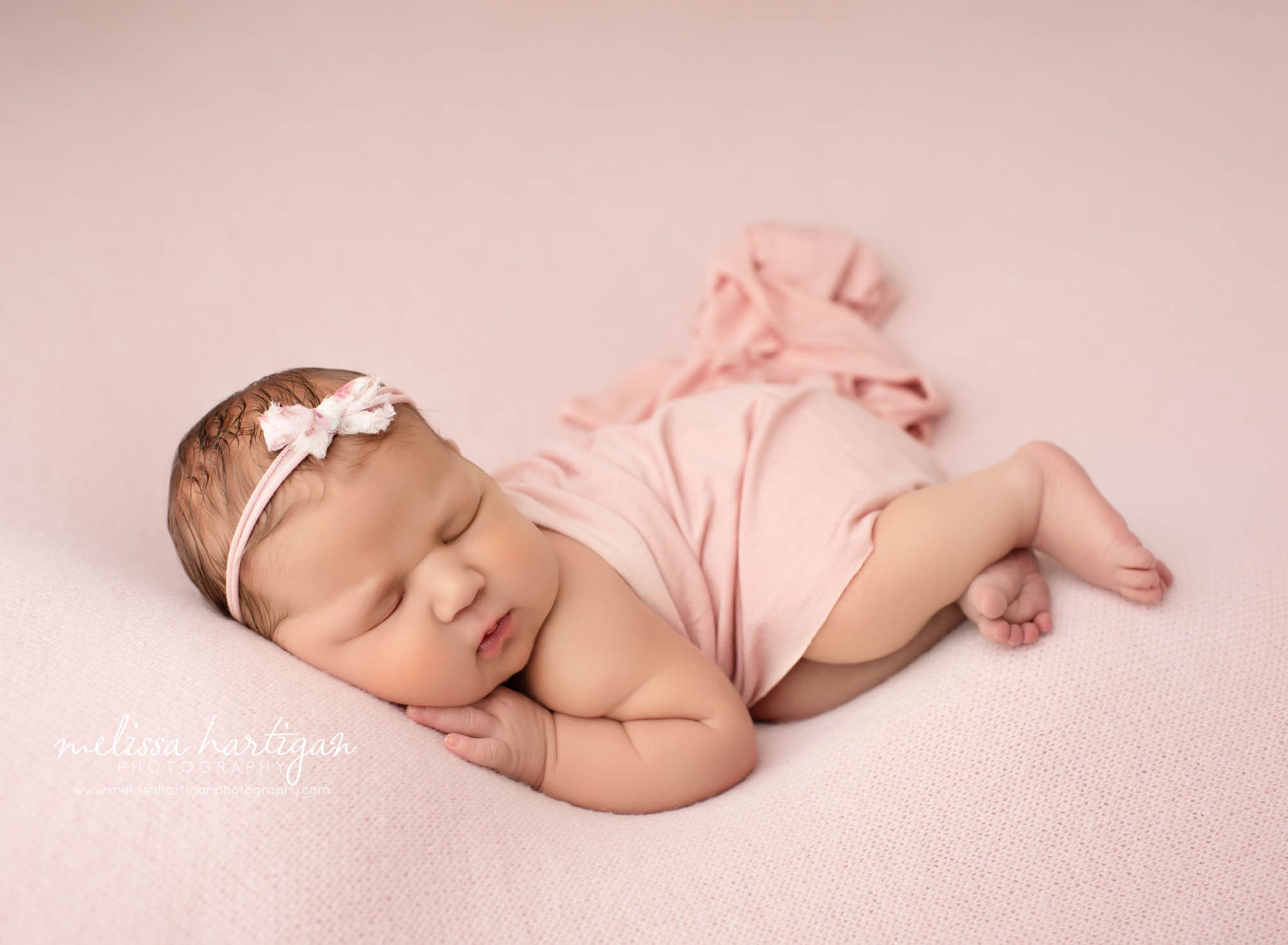 newborn baby girl posed on side with pink bow and pink layer draped over newborn photography hartford county