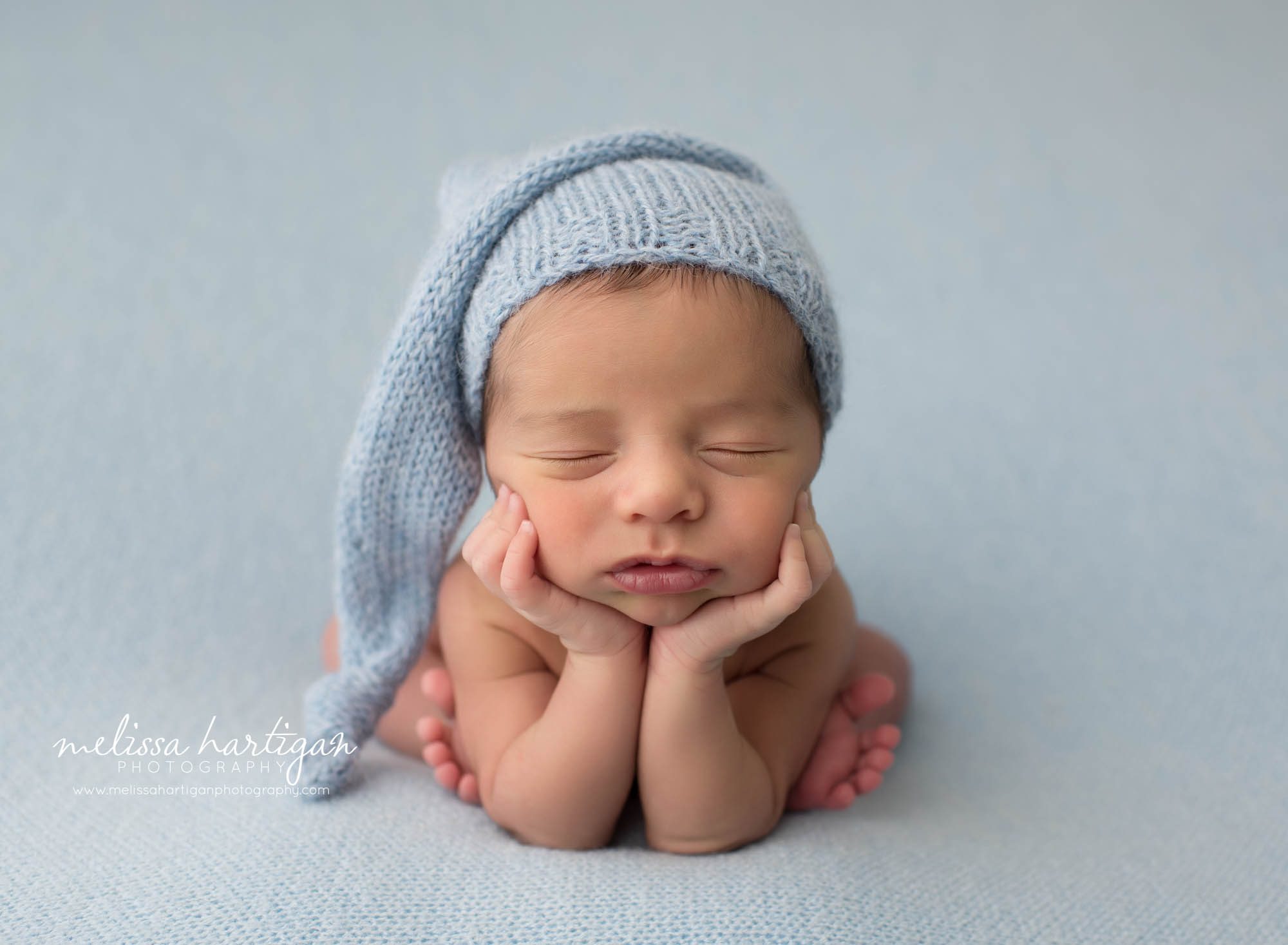 newborn baby boy posed froggy pose wearing knitted blue sleepy cap