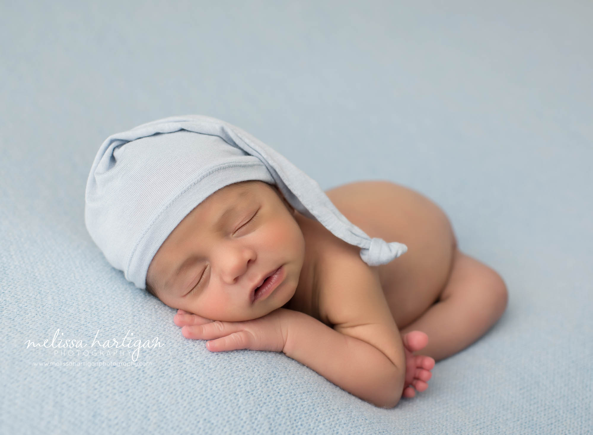 newborn baby boy posed modified taco pose wearing sleepy cap