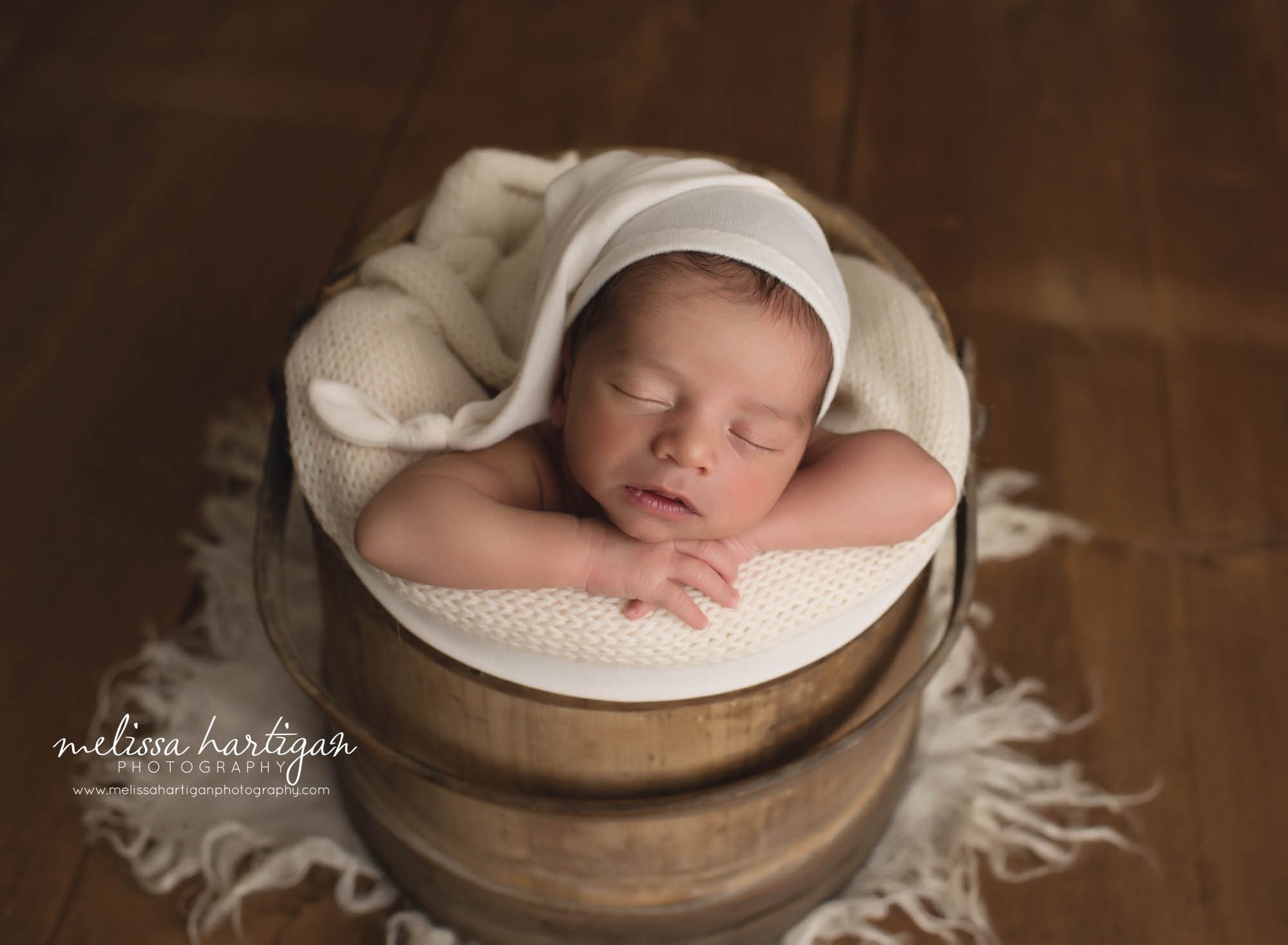 newborn baby boy posed in wooden barrel bucket with cream sleepy cap and cream knitted layer