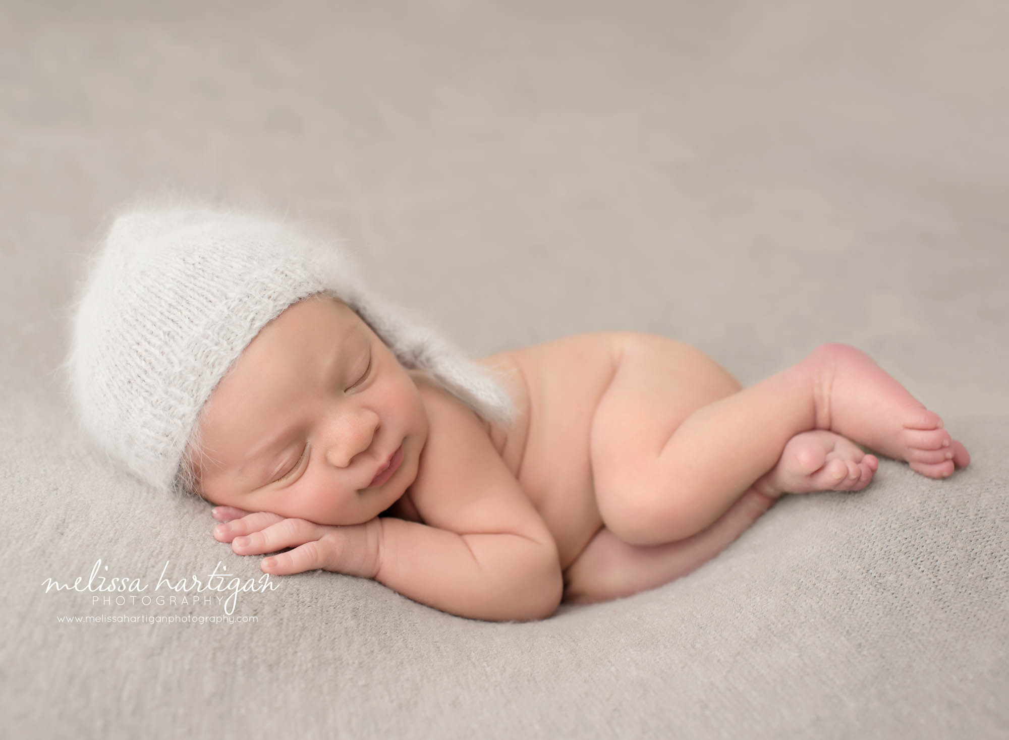 sweet baby boy posed on side on light gray backdrop wearing knitted gray sleepy cap CT newborn Photographer