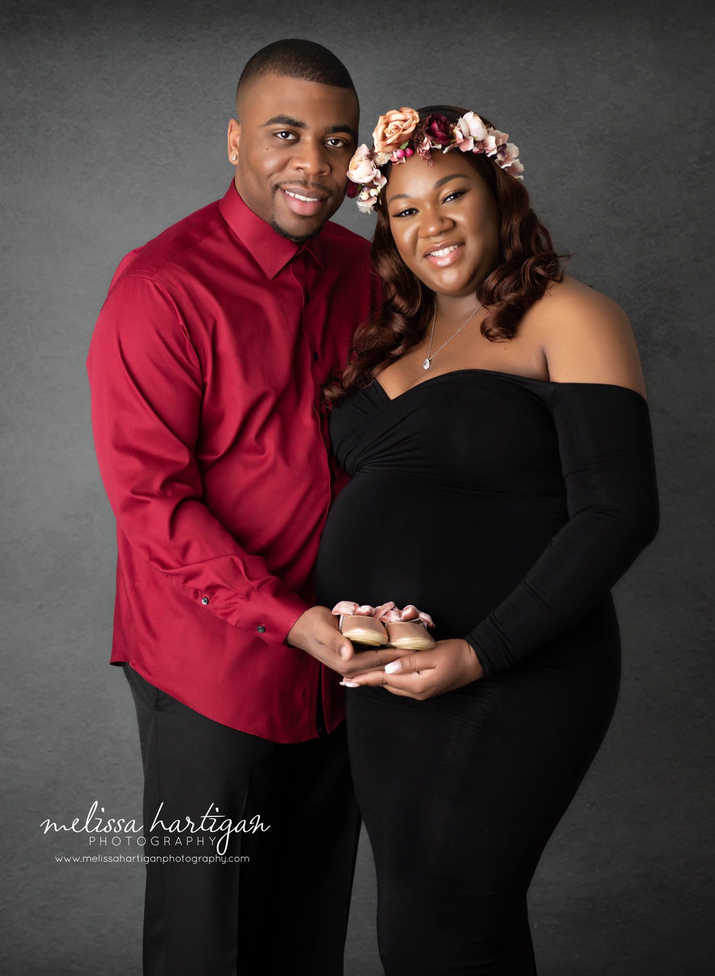 expectant couple holding newborn baby girl shoes in maternity photography session Massachusetts